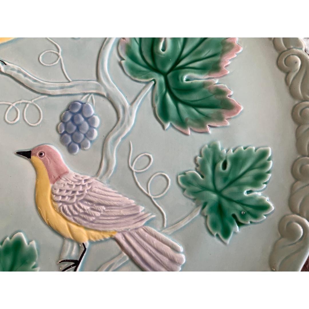 Excellent condition! Pale blue Majolica plate is decorated with 2 raised pink & yellow birds resting on grape vines with green leafs; decorative boarder around edge of plate with stylized design; great vivid colors for age; perfect addition as a