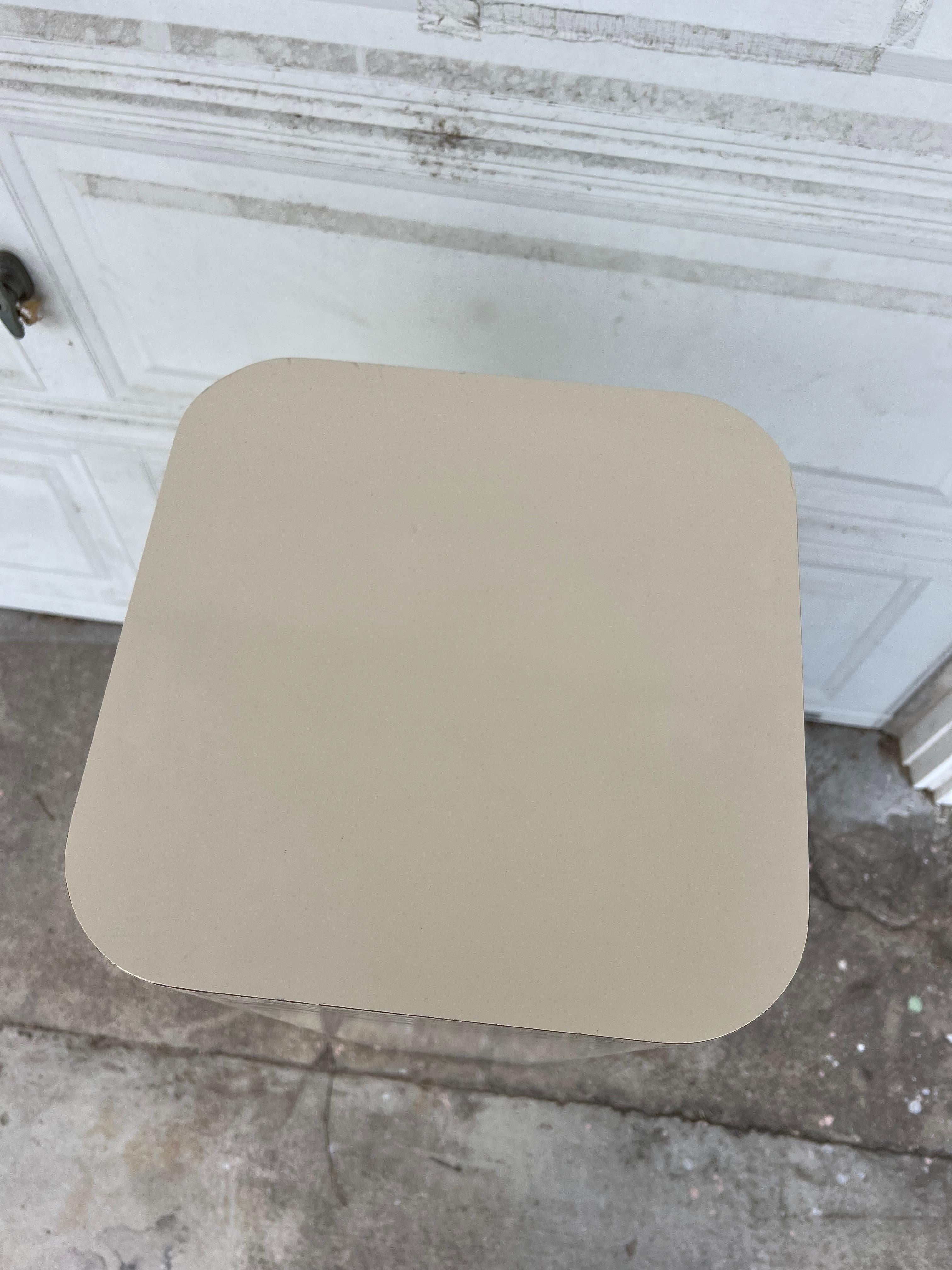 Sleek ivory laminate pedestal stand approximately 42” high. Rounded edges on the square’s corners. Overall very good vintage condition, minimal scrapes or chips- please see all media in posting for any flaws. Metal (chrome) feet attached on the