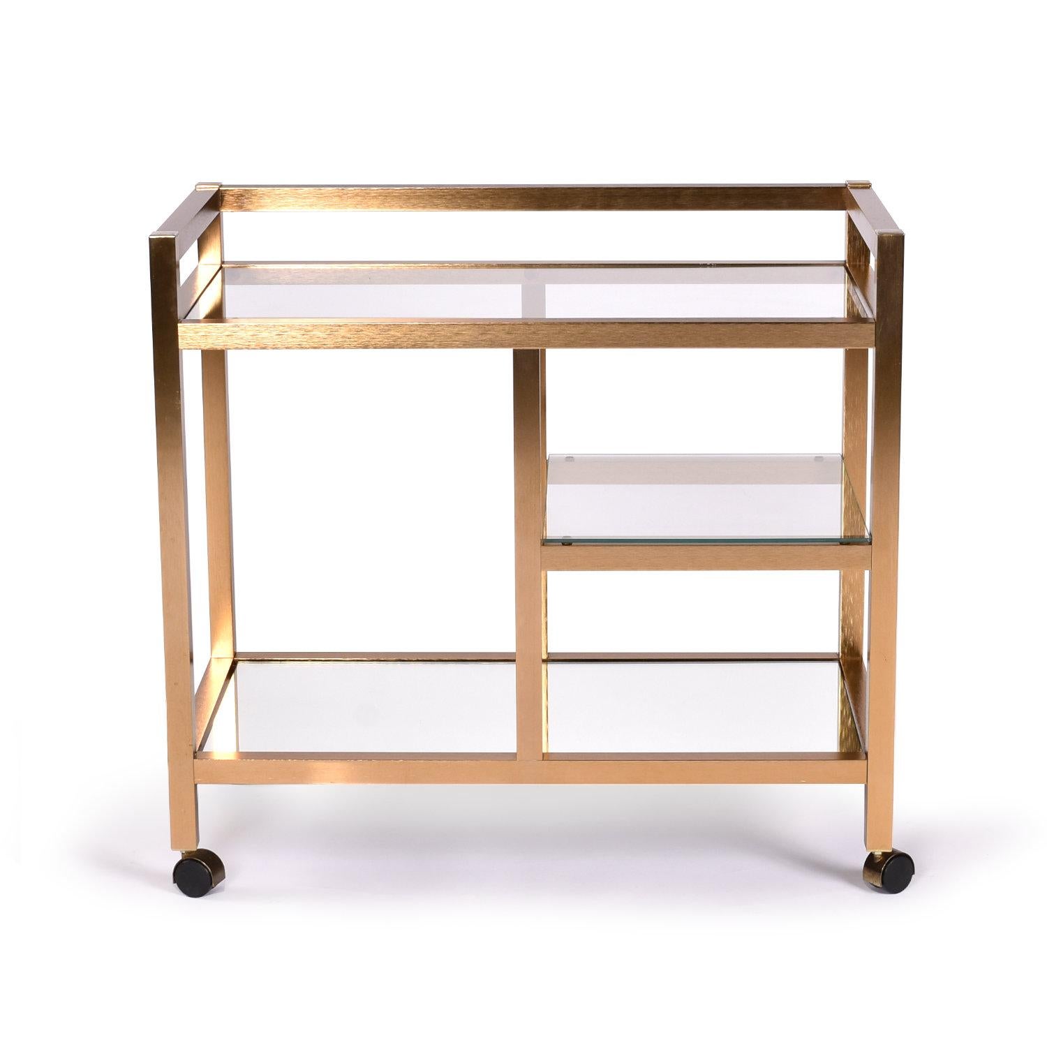 Stunning Nineteen-Laties vintage gold colored bar cart with glass shelves and mirror bottom. The distinctive cart has an atypical warm-copper tint to the metallic gold finish. Take a close look at the frame to see that the metal is actually textured