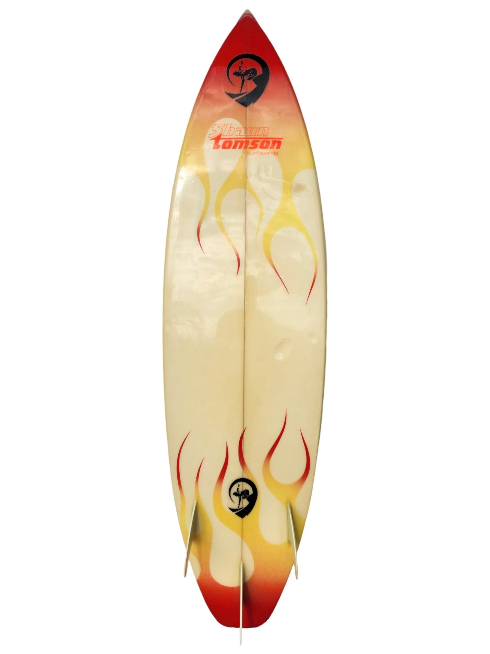 Mid-1980s Vintage Shaun Tomson surfboard made by Donald Kadowaki. Features flaming airbrush design, fixed thruster (tr-fin) setup, and squash tail. A remarkable example of a 1980s surfboard shaped under the renowned Shaun Tomson label, created by