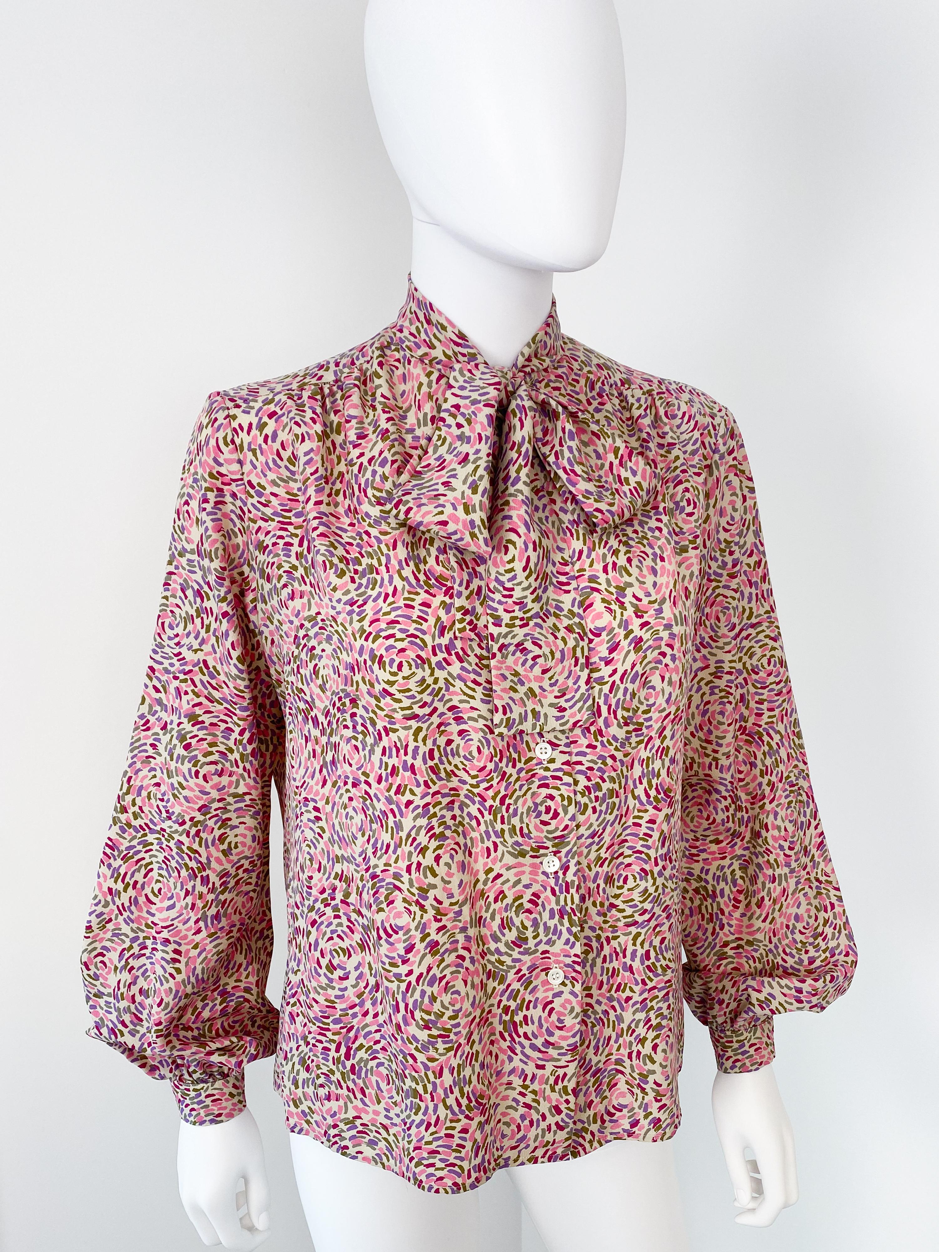 Wonderful vintage 1980s silky polyester pussy bow blouse with original tie. Pointillism print pattern in pink, purple, burgundy, and green colors over an off-white background. Long sleeves shape with ample pleating at the button cuffs to provide
