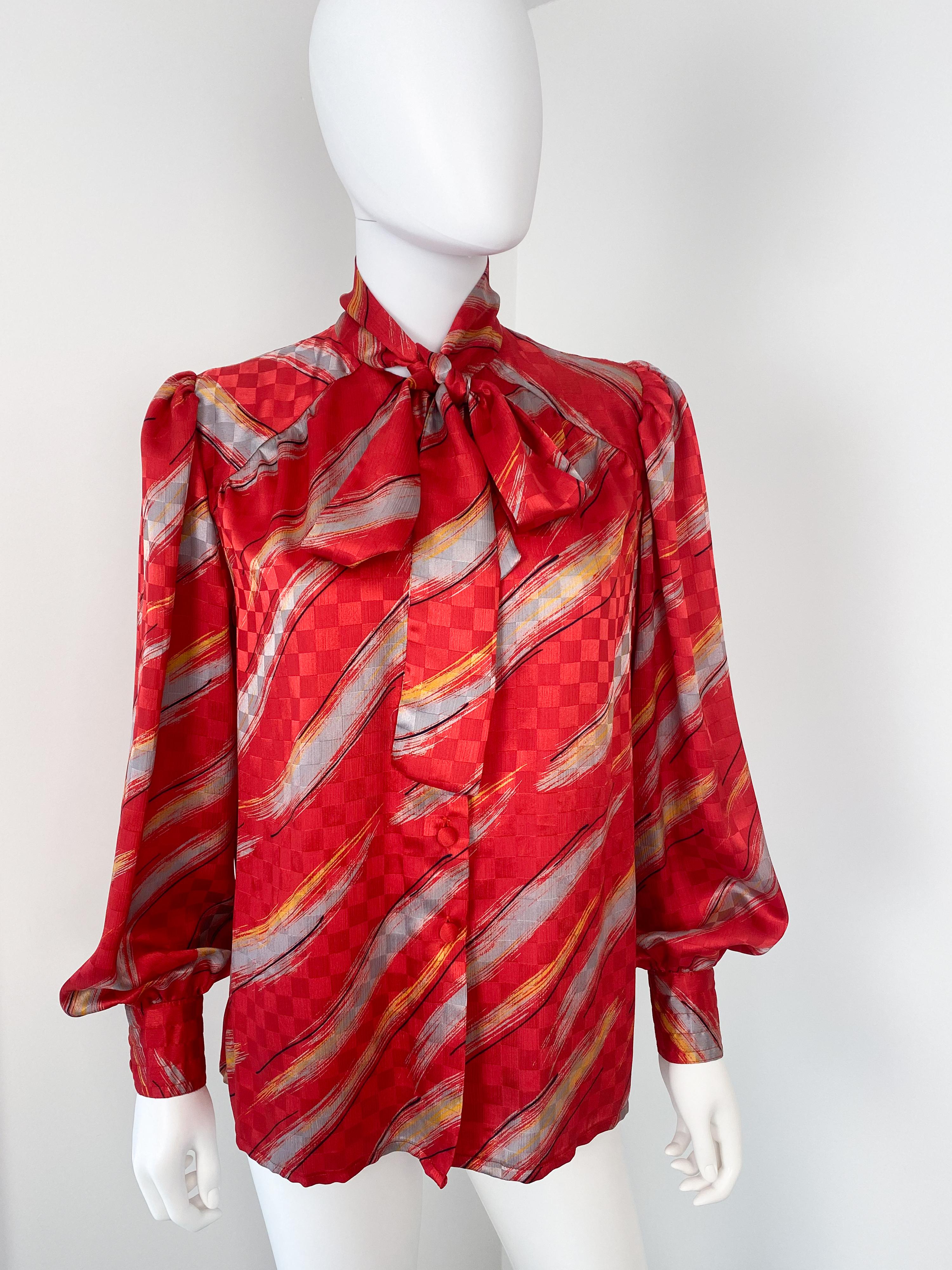 Wonderful vintage 1980s silky polyester pussy bow blouse with attached bow-scarf. Bright red colors fabric with slash pattern in gray and yellow colors with black contrast. The fabric has a shiny checkerboard textured finish. 
There is ample