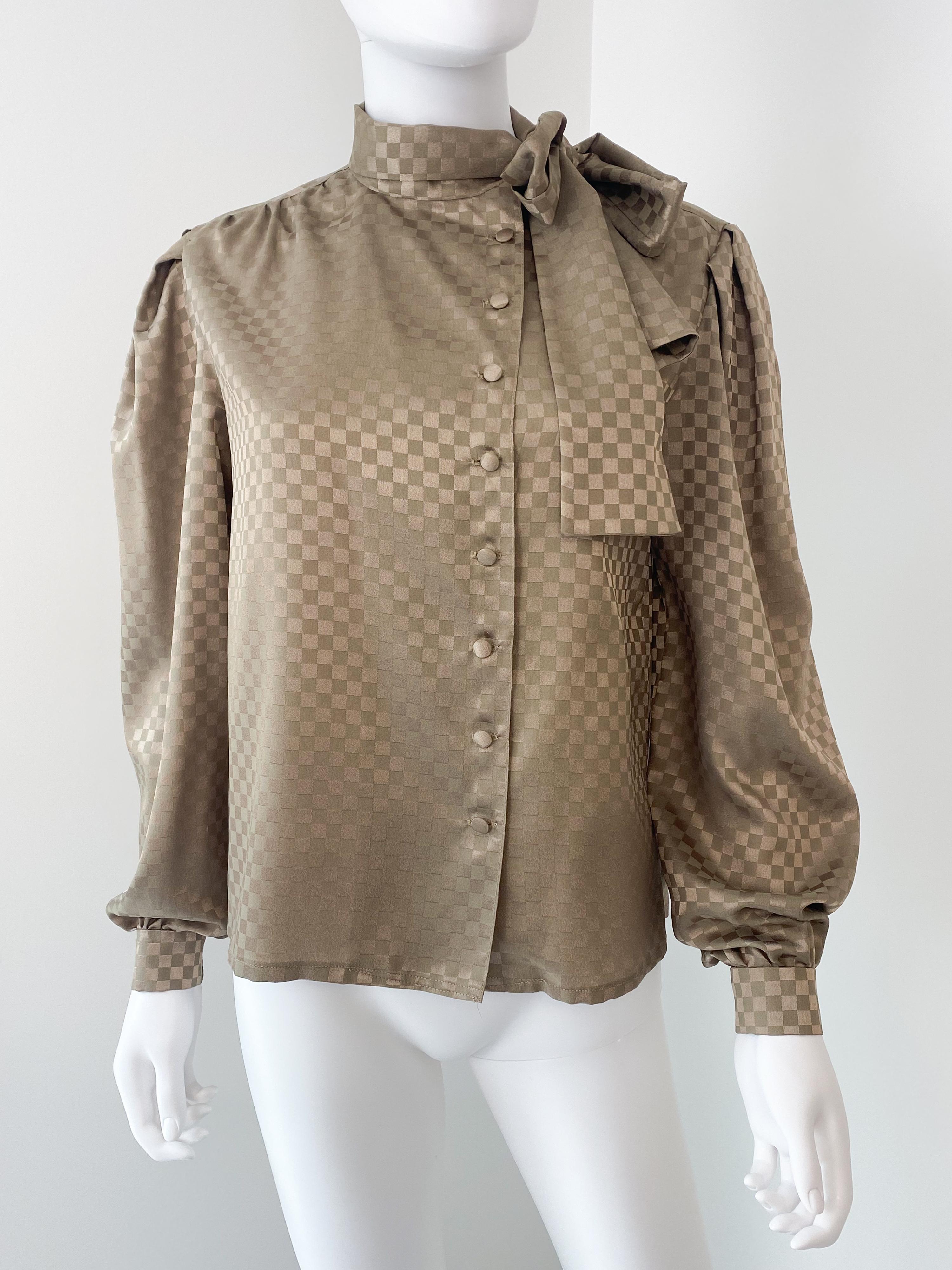 Splendida camicetta vintage anni '80 in poliestere setoso con fiocco a foulard. Tessuto vibrante color tortilla con motivo geometrico a scacchiera tono su tono. Le spalle e i polsini con bottoni sono ampiamente pieghettati per dare volume. Il fiocco