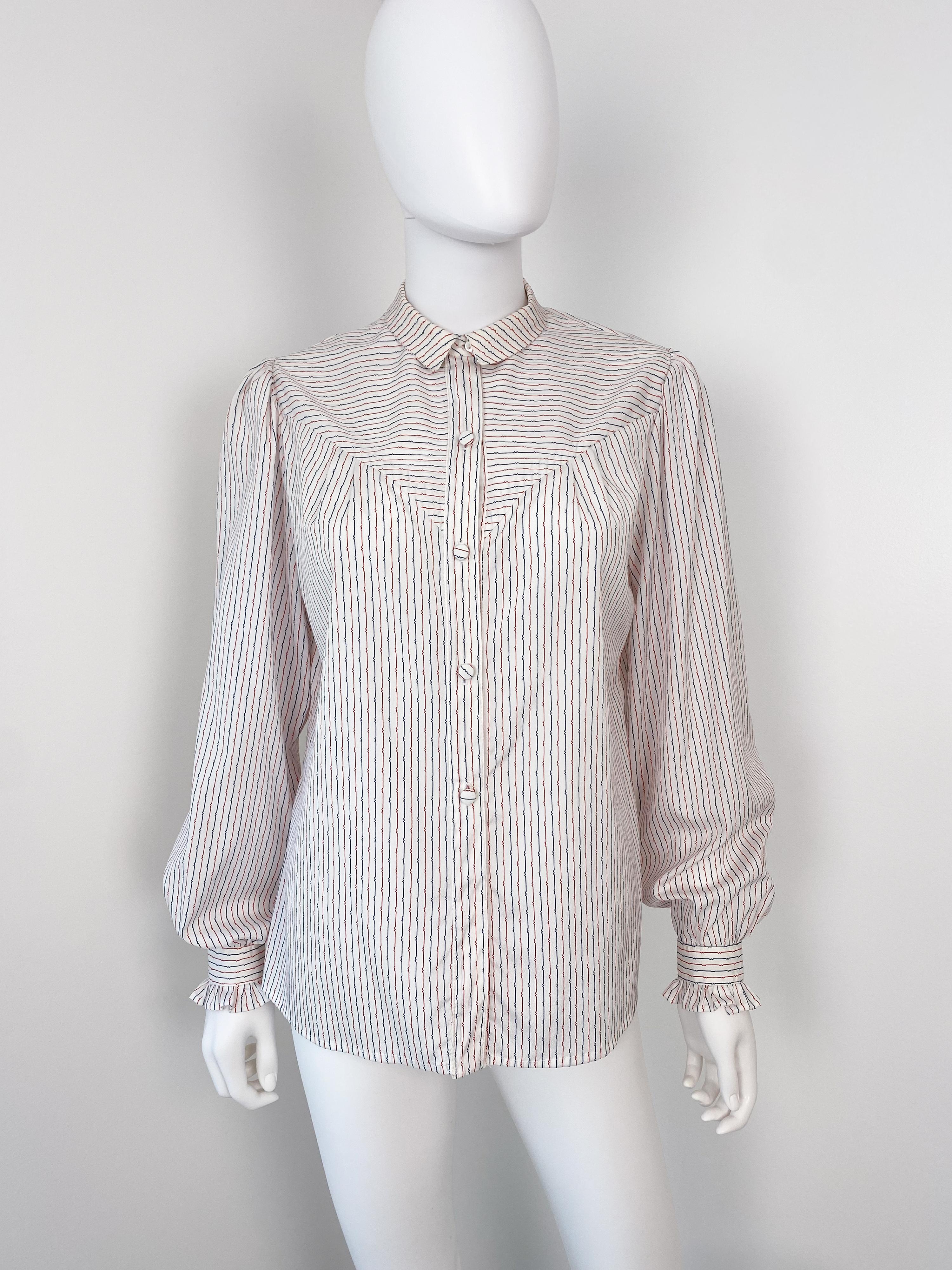 Wonderful vintage 1980s silky polyester western-style blouse. White color fabric with striped pattern in red and blue colors. Contrasting fabric insert on the chest and back. Romantic fabric ruffles at the button cuffs. There is gentle pleating at