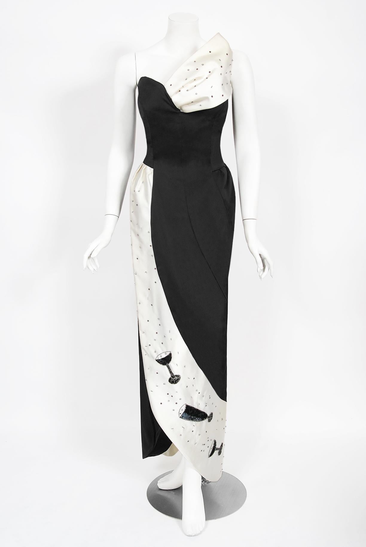 Une robe fantaisiste et totalement unique en son genre, en satin noir et blanc, signée Tan Giudicelli, de Paris, avec des flûtes de champagne et des bulles pailletées. Il était connu pour son approche surréaliste de la mode et cette robe ne fait pas
