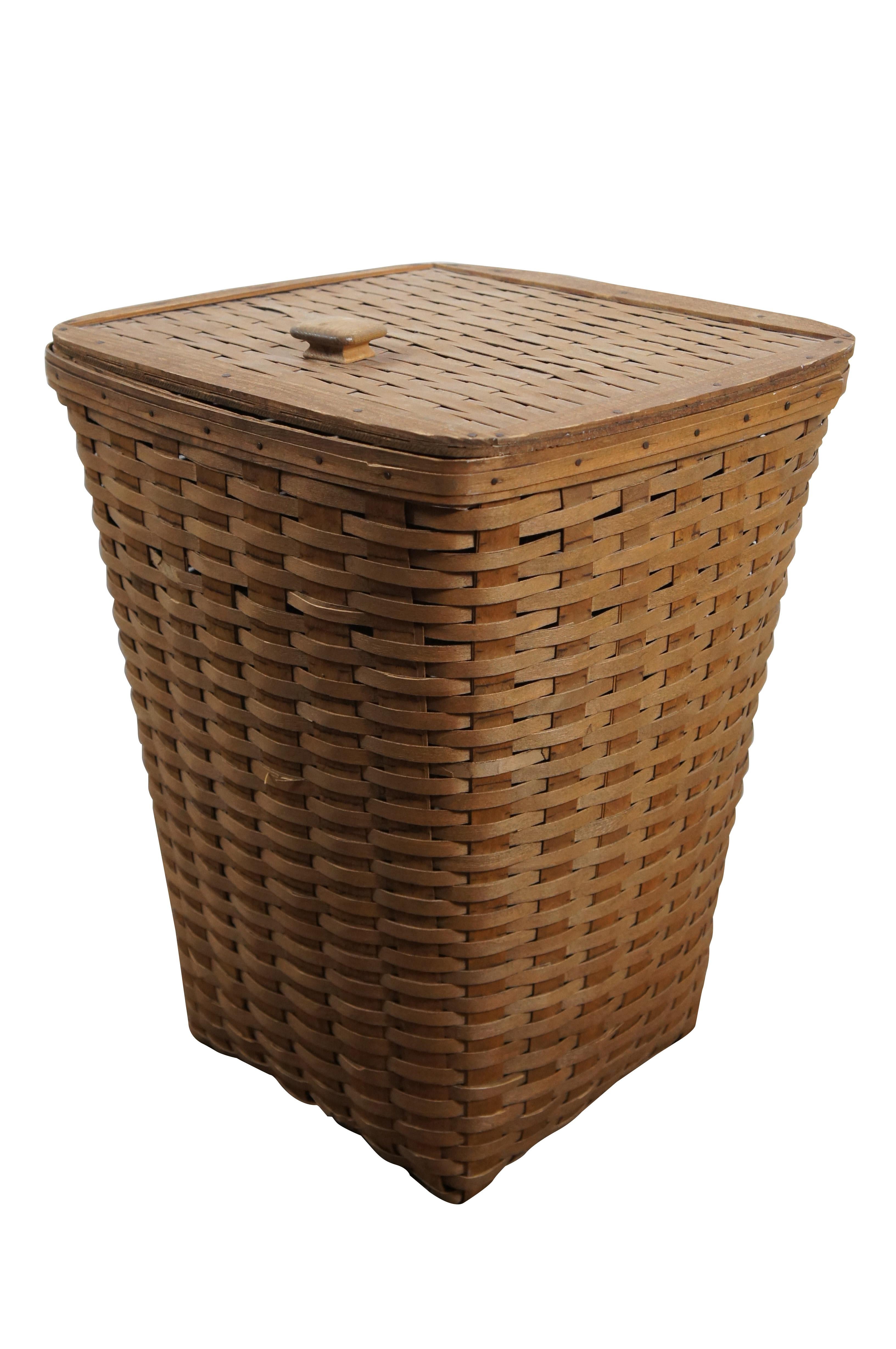 Vintage 1983 Longaberger hand woven maple laundry basket / clothes hamper / trash can featuring a square form with tapered base and lid with square handle attached with leather strap hinges. Signed SAC 83.

“The Longaberger Company was an American