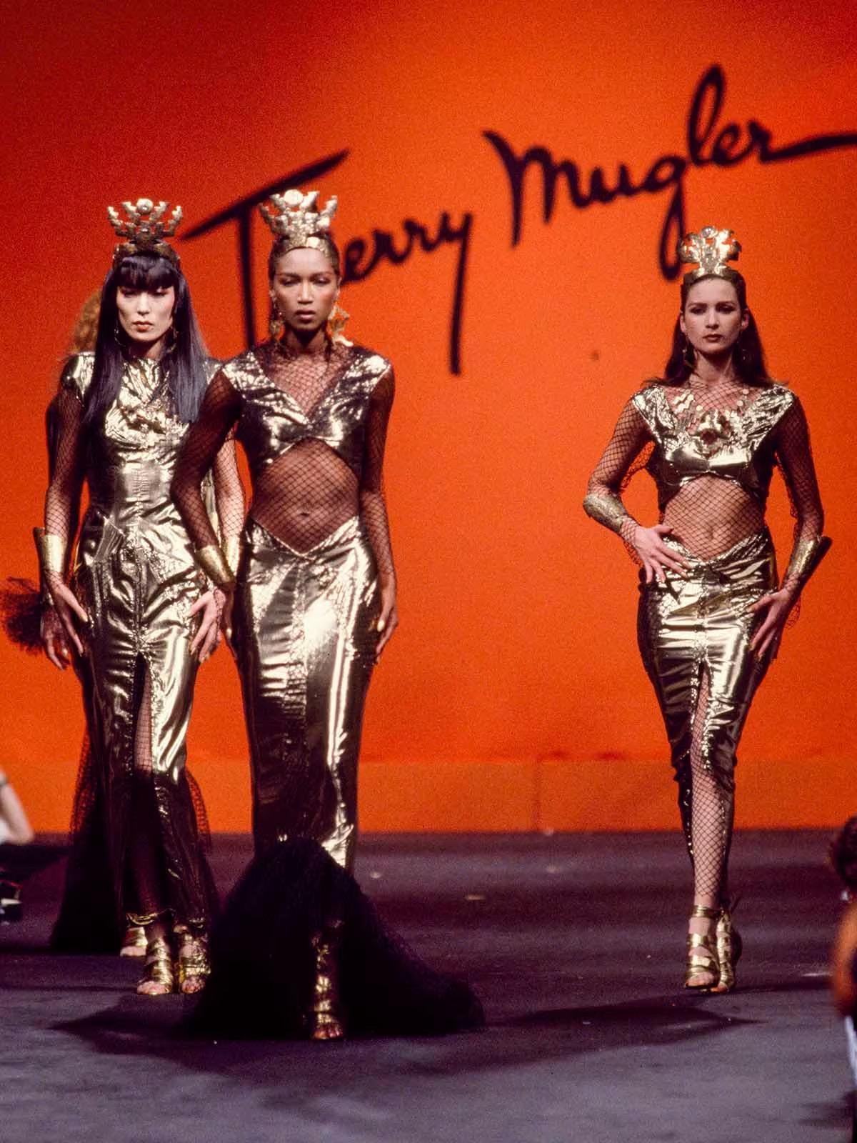 An iconic and highly coveted Thierry Mugler couture metallic gold lamé and fishnet hourglass gown dating back to his documented 1985 spring/summer collection. Garments from this show are next to impossible to find. This legendary French fashion