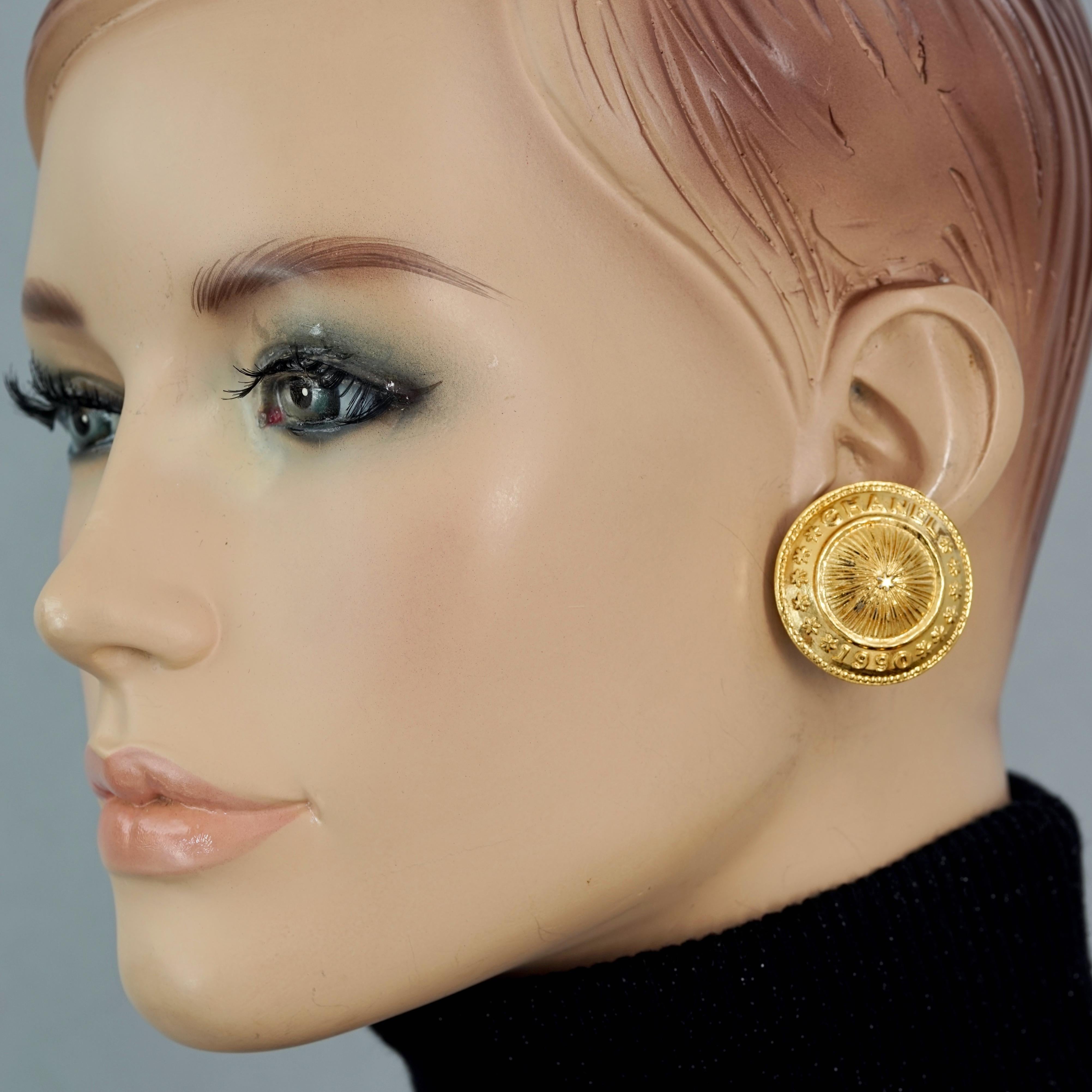 Vintage 1990 CHANEL Logo Sunburst Medallion Disc Earrings

Measurements:
Height: 1.22 inches (3.1 cm)
Width: 1.22 inches (3.1 cm)
Weight per Earring: 11 gram

Features:
- 100% Authentic CHANEL.
- Medallion/ Disc/ Coin earrings with embossed CHANEL