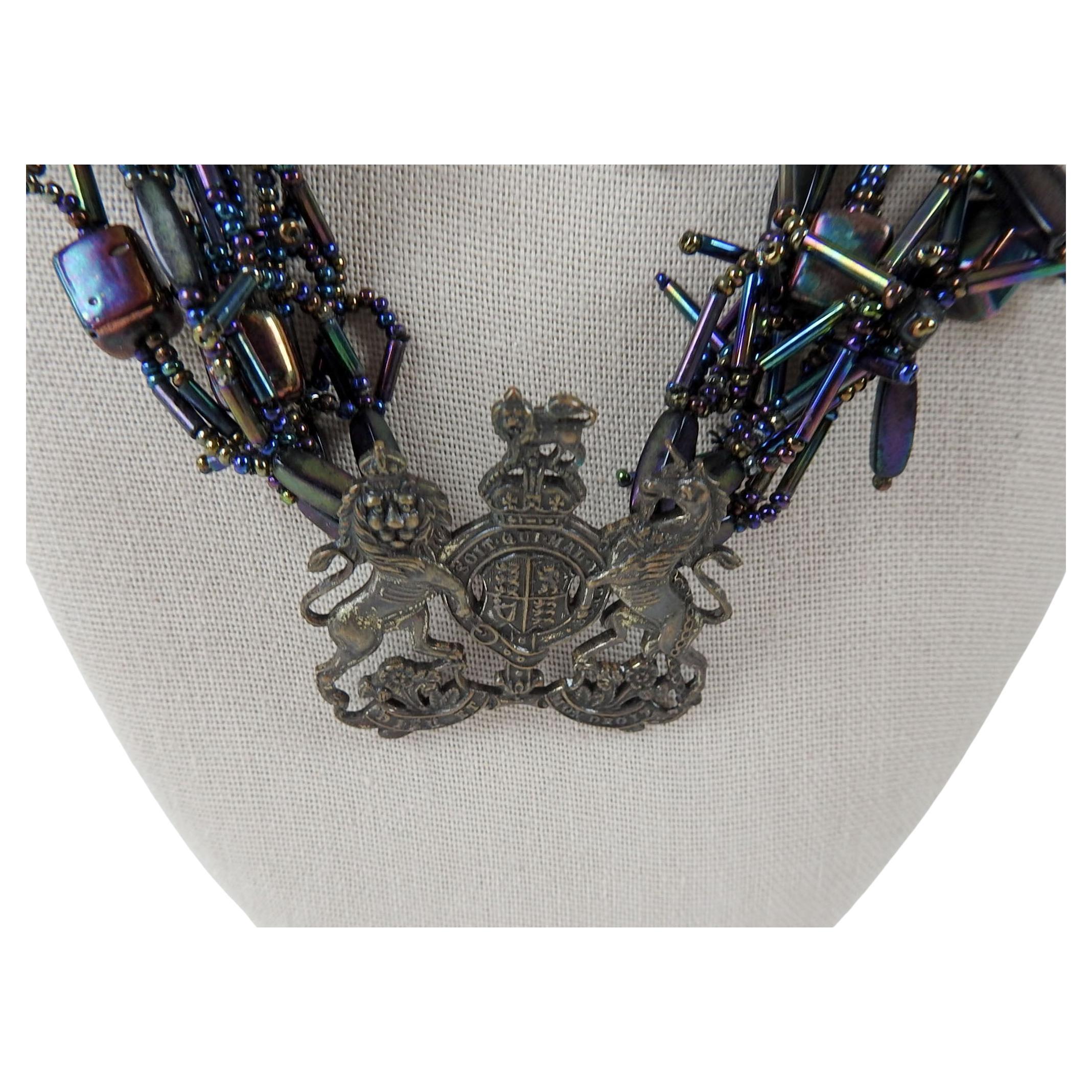 1990's Artist studio made multistrand beaded necklace using purple iridescent beads of various shapes and vintage brass British royal crest. By Linda Thompson (20th/21st century) Texas, 20