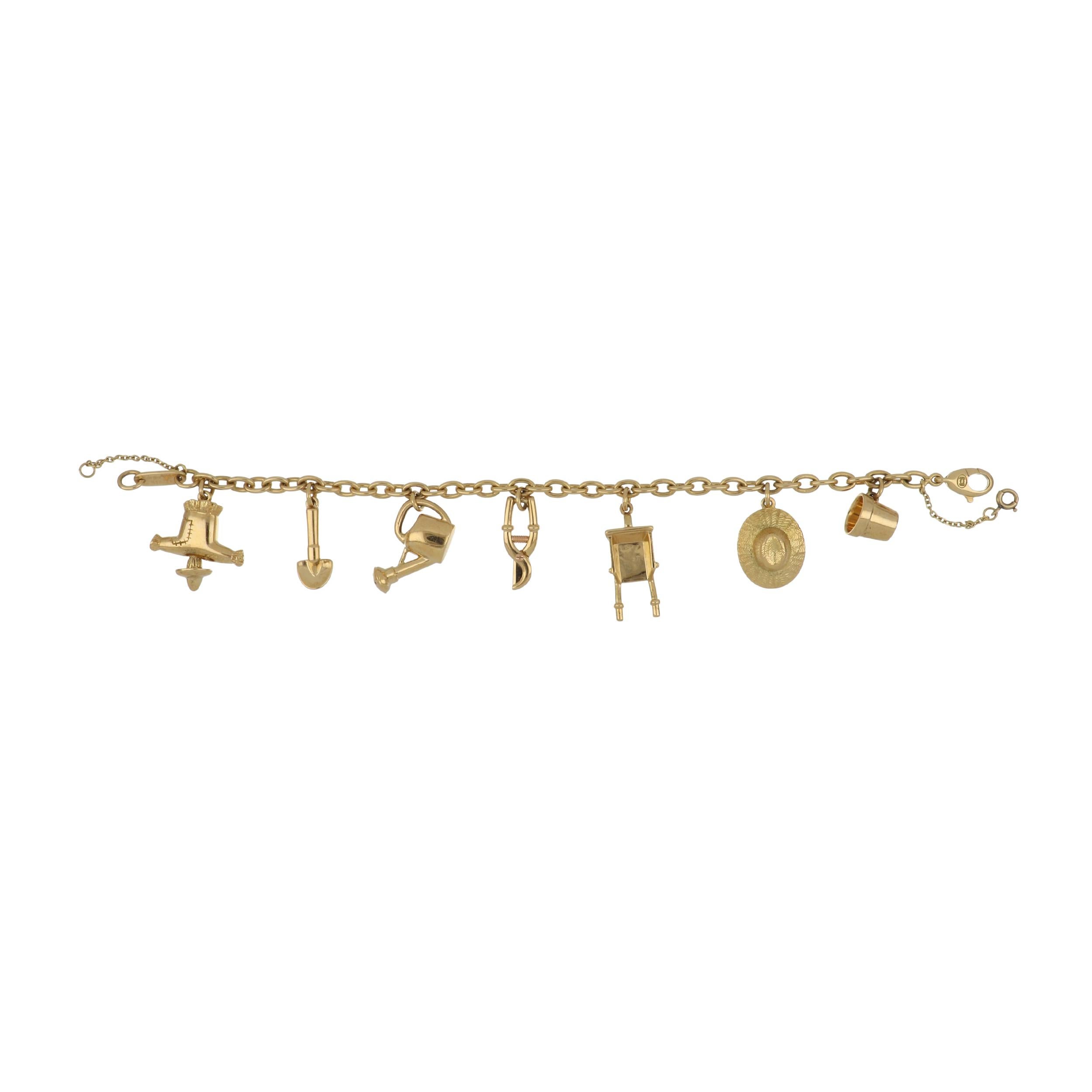 A vintage Cartier 18K yellow gold charm bracelet with gardener motif charms. Charms include a scarecrow, spade, watering can, pruning shears, wheel barrow, wide-brimmed hat, and a flower pot. Dated 1994. The bracelet measures 7 inches in length with