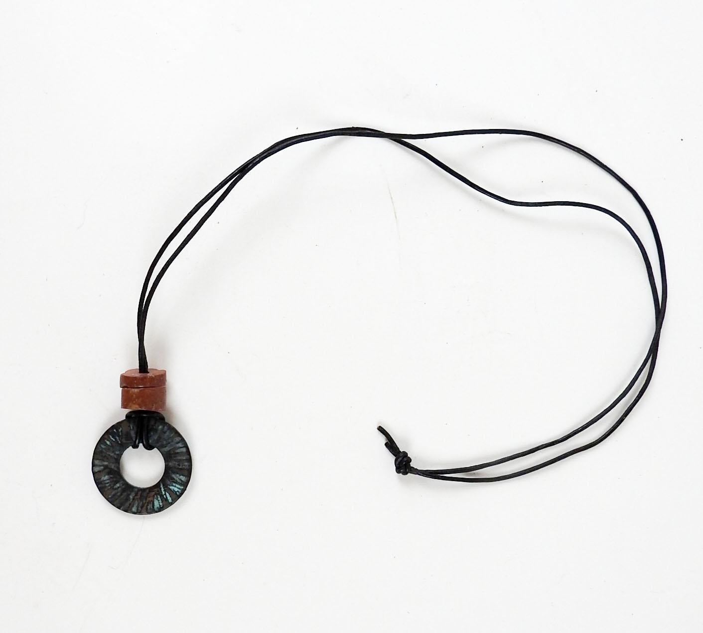 Circa 1990's hammered patinated bronze circle with bauxite bead accent. On thin round black leather cord, pendent is 1.25