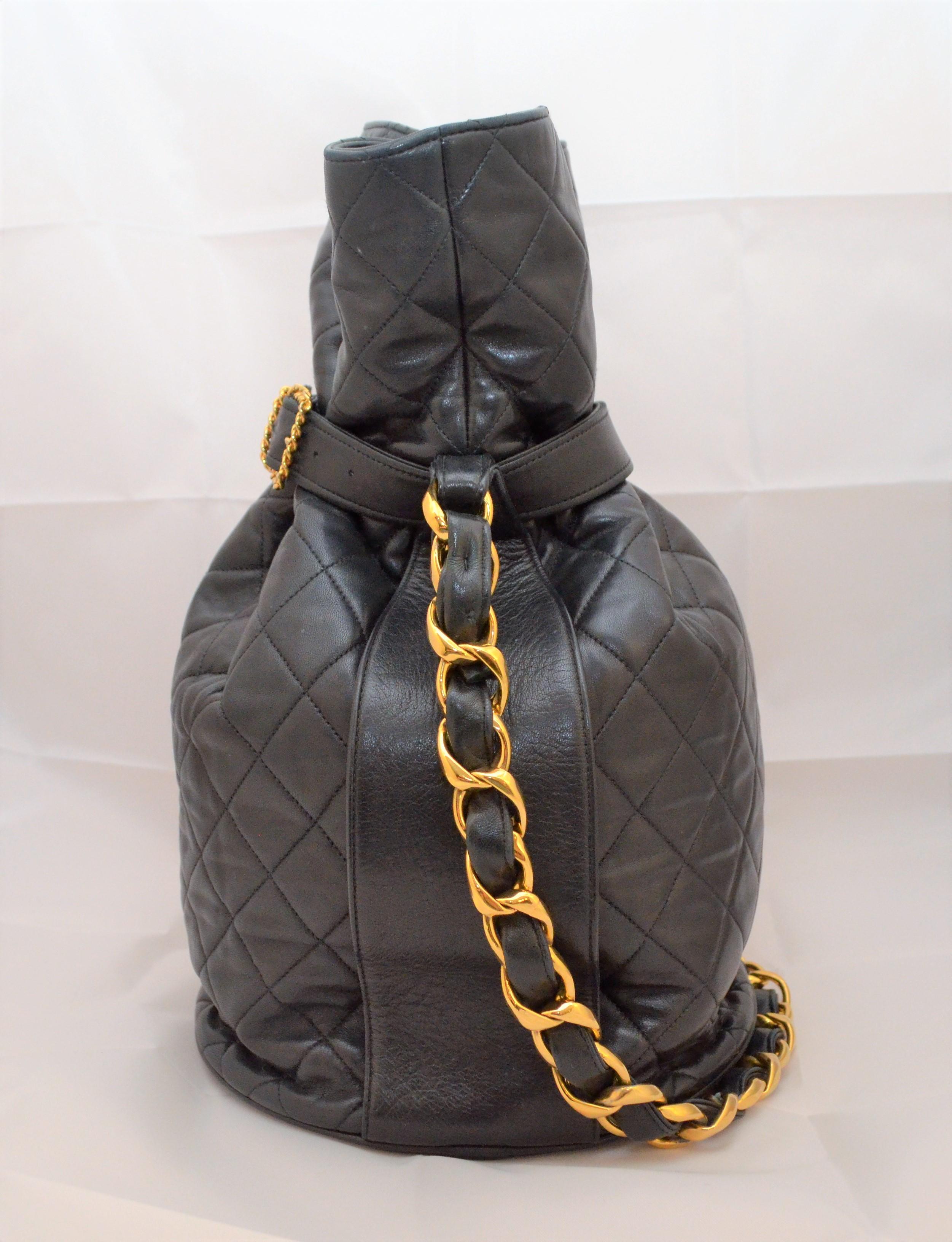 Vintage Chanel tote features black quilted leather throughout with a gold-tone metal chain and leather top handle and buckle fastening. Interior is fully lined in a jacquard fabric. Base of the tote bag has a signature embossed CC logo. Made in