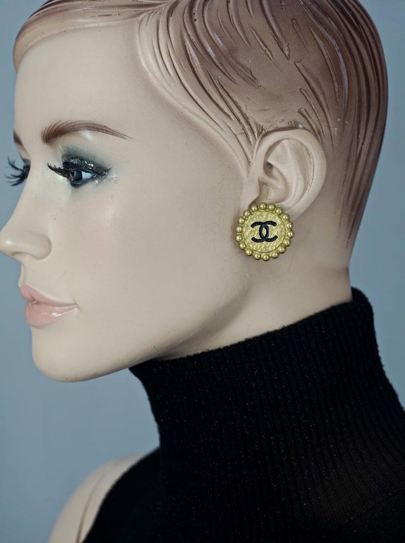 Vintage 1994 CHANEL CC Logo Flower Earrings

Measurements:
Height: 1.06 inches (2.7 cm)
Width: 1.06 inches (2.7 cm)
Weight per Earring: 8 grams

Features:
- 100% Authentic CHANEL.
- Flower earrings with Chanel CC logo in black enamel.
- Patinated
