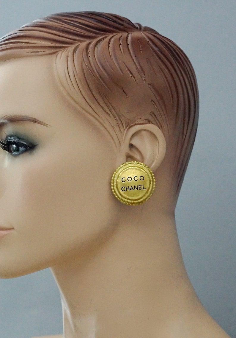 Vintage 1994 COCO CHANEL Medallion Disc Earrings

Measurements:
Height: 1.29 inches (3.3 cm)
Width: 1.29 inches (3.3 cm)
Weight per Earring: 15 grams

Features:
- 100% Authentic CHANEL.
- Disc medallion earrings with engraved COCO CHANEL at the