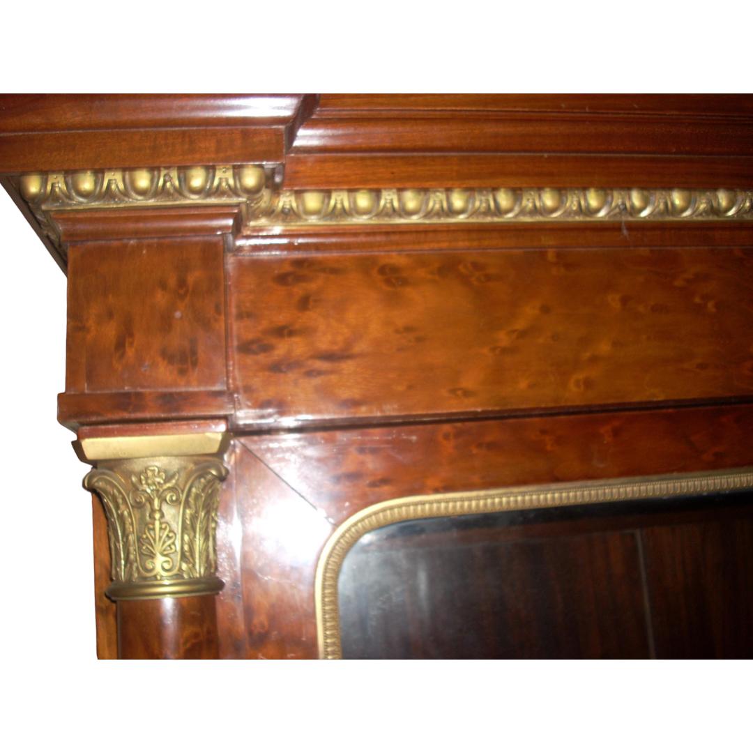 Solid mahogany with birdseye maple veneer on exterior; stepped molded cornice with egg and dart gilt wood trim; Corinthian gilt wood pilaster capitals, gilt brass hardware and window trim; two adjustable shelves behind two glass doors in upper