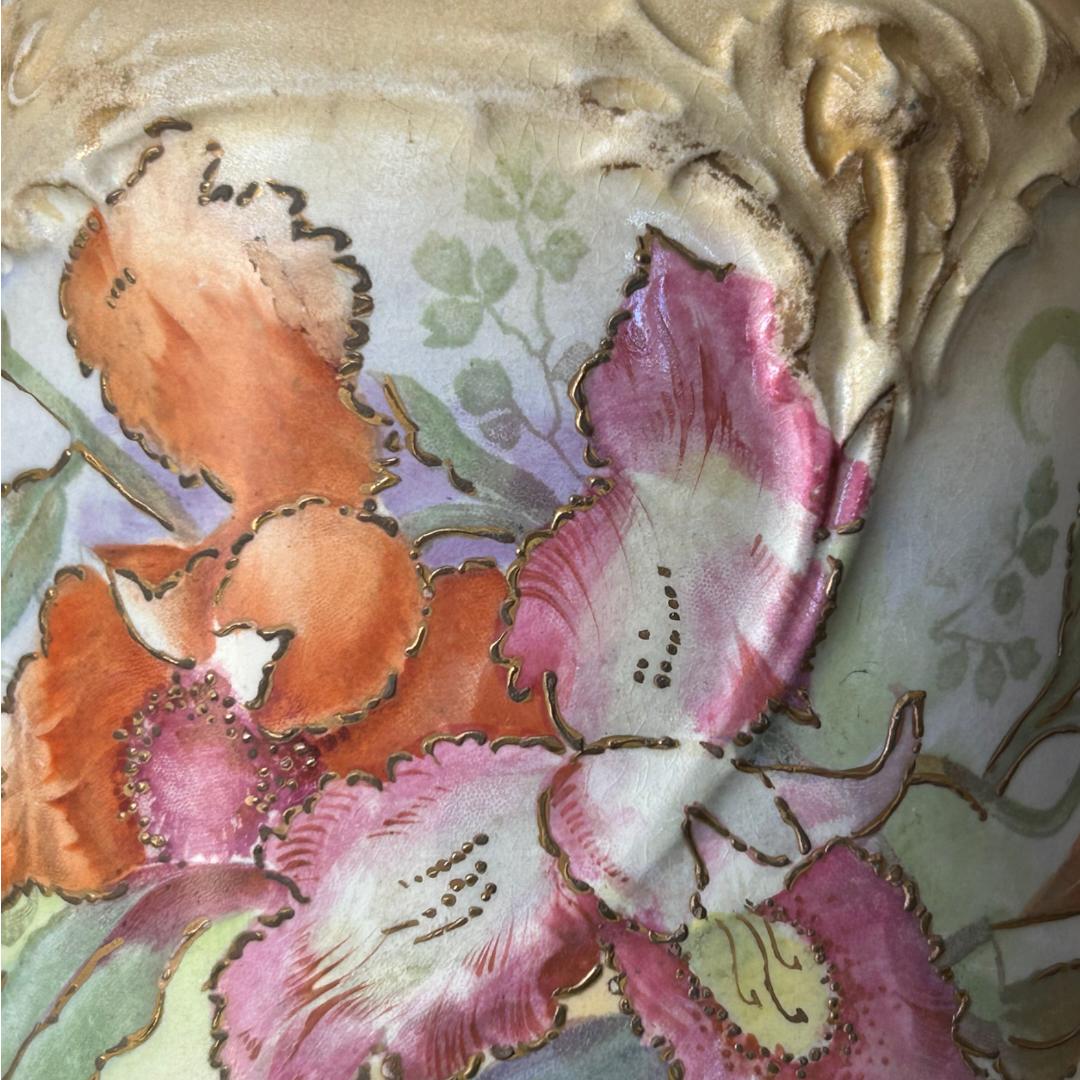 Diese schöne Vintage-Keksdose ist ein wahrer Schatz für jeden Sammler.  Sie wurde im 19. Jahrhundert von Royal Bonn hergestellt und zeigt eine wunderschöne mehrfarbige Catleya-Orchidee mit einem erhabenen Muster aus Distelblüten und Blättern auf