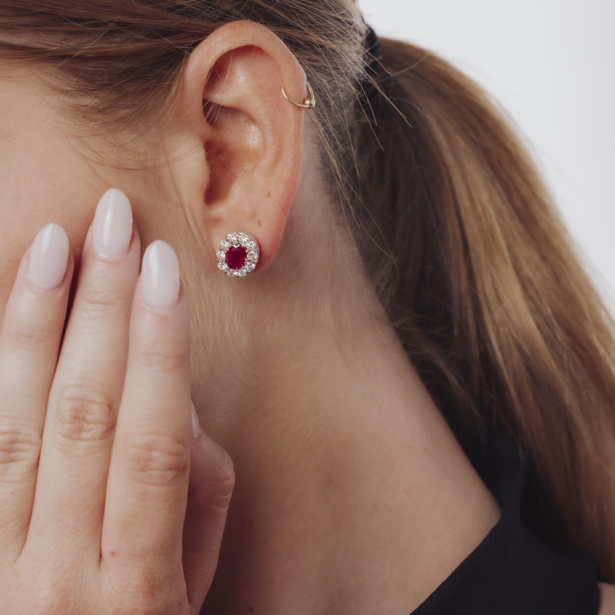 Estos pendientes vintage de los años 80 están elaborados en platino y presentan dos rubíes de talla ovalada con un peso combinado de aproximadamente 2 quilates. Alrededor de los rubíes hay veinte diamantes redondos de talla brillante, con un total