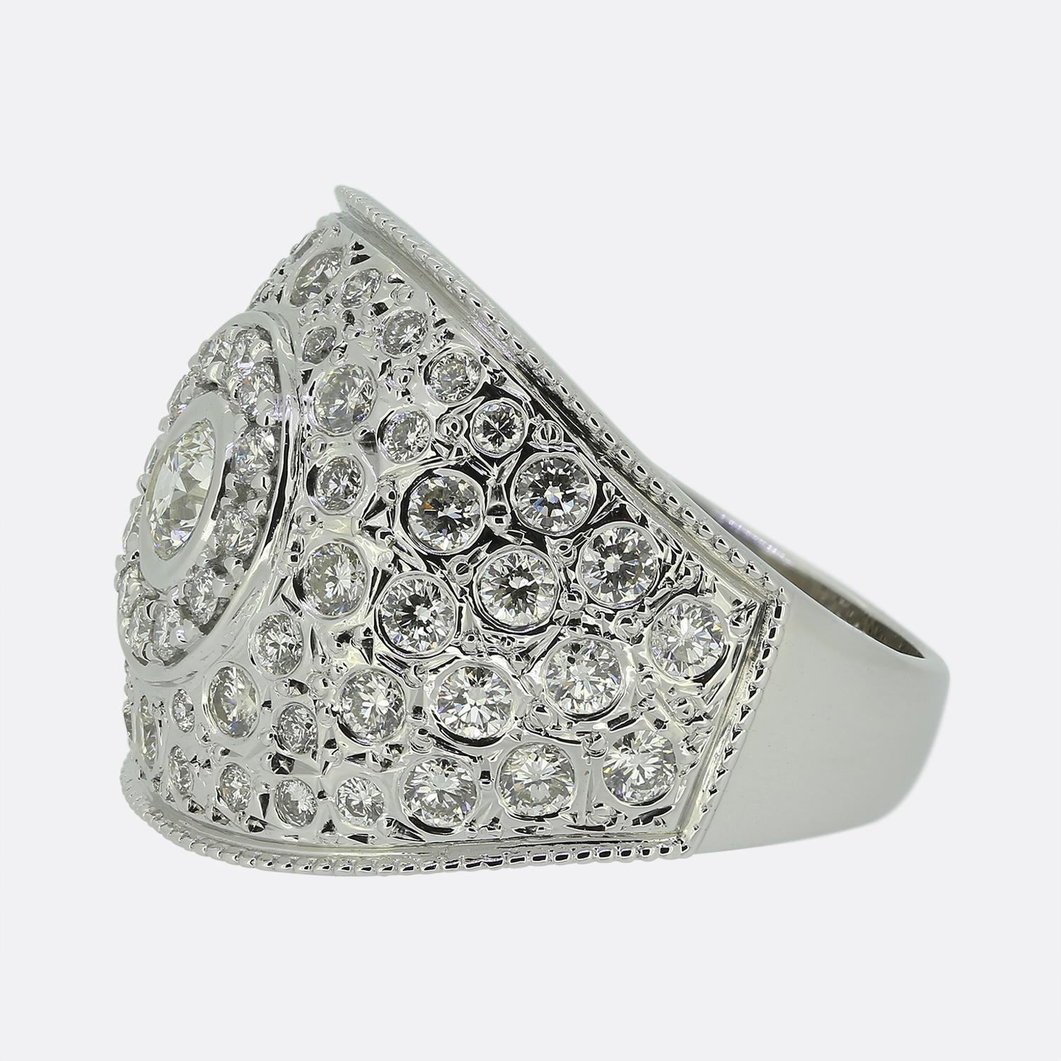 Hier haben wir einen großen Diamant-Cluster-Ring aus 18 Karat Weißgold. Der Ring besteht aus einem runden Brillanten von 0,35 Karat in der Mitte, der durch Reiben gefasst und von einer Gruppe von über 50 passenden kleineren Steinen umgeben ist.