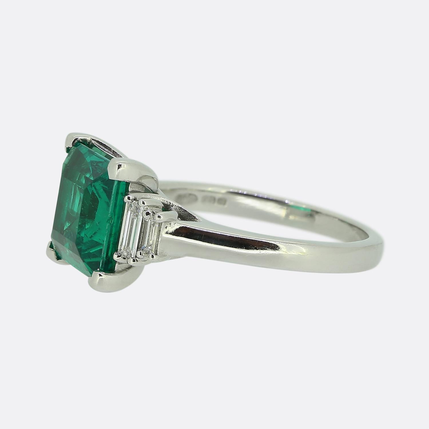 Here we have a stunning emerald and diamond ring. This vintage piece has been crafted from platinum and features a square shaped two carat natural emerald possessing a vibrant electric green medium tone. This principal stone sits slightly risen in a