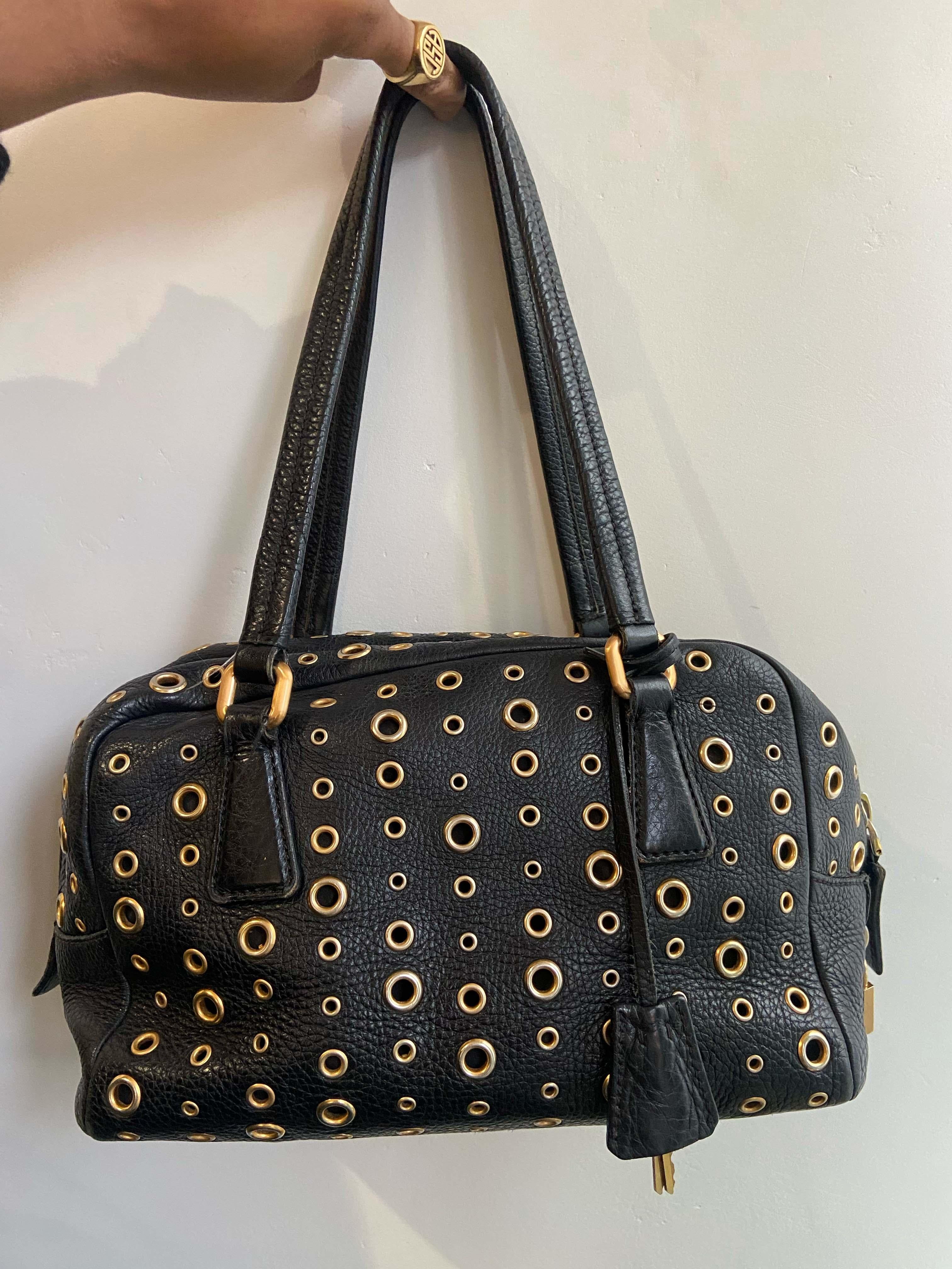 Vintage Prada 2000's Grommet Bauletto, bag. Features black leather with gold eyelets allover, gold tag lock and key. Inner zip back pocket. Leather straps. Fastens with zip closure. 

Brand: Prada
Color: Black&Gold
Fabric: Leather
Year / Season: