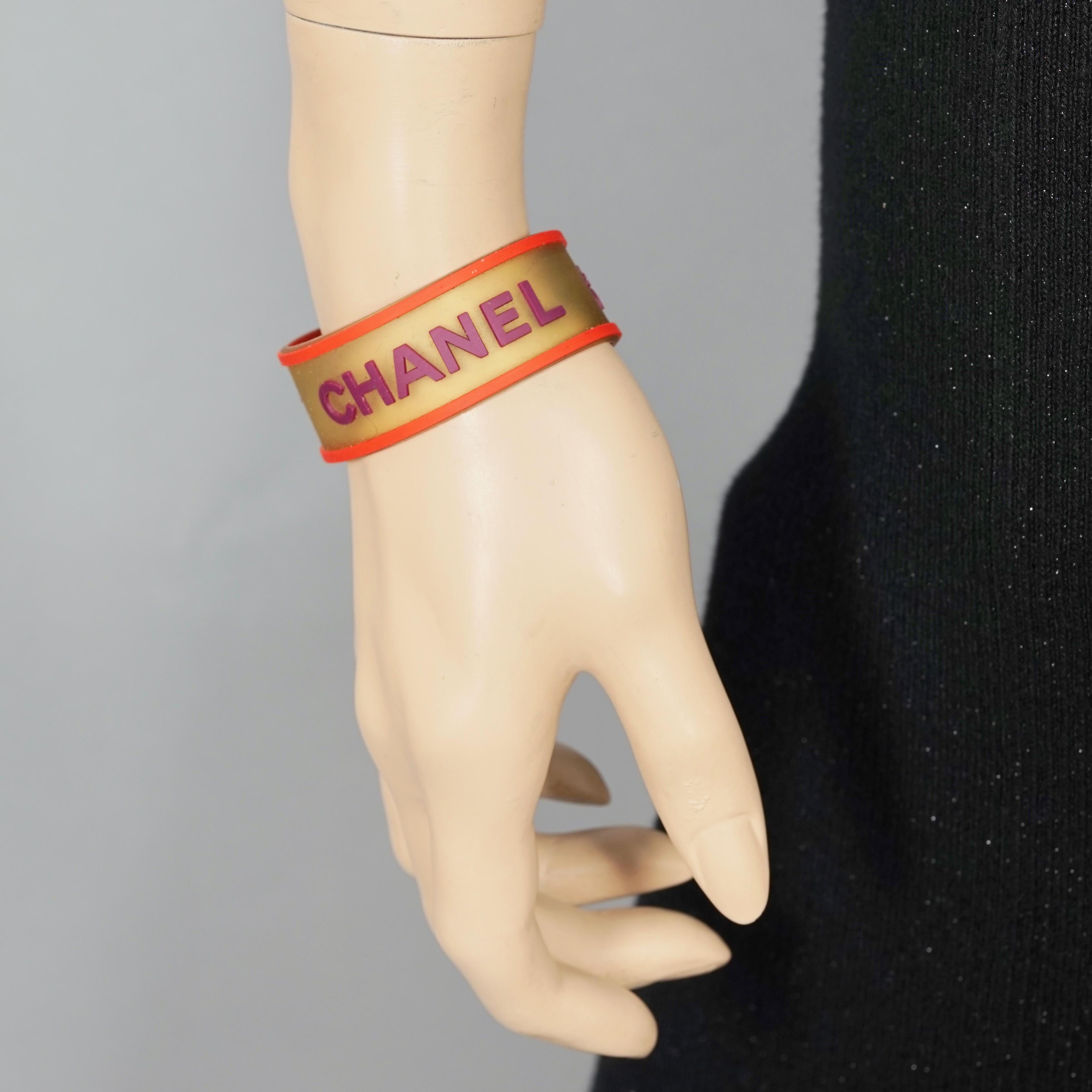 Vintage 2001 CHANEL Logo Camellia Orange Violet Rubber Cuff Bracelet

Measurements:
Height: 0.86 inch (2.2 cm)
Circumference: 7.28 inches (18.5 cm)

Features:
- 100% Authentic CHANEL.
- Translucent orange and violet rubber with embossed CHANEL and