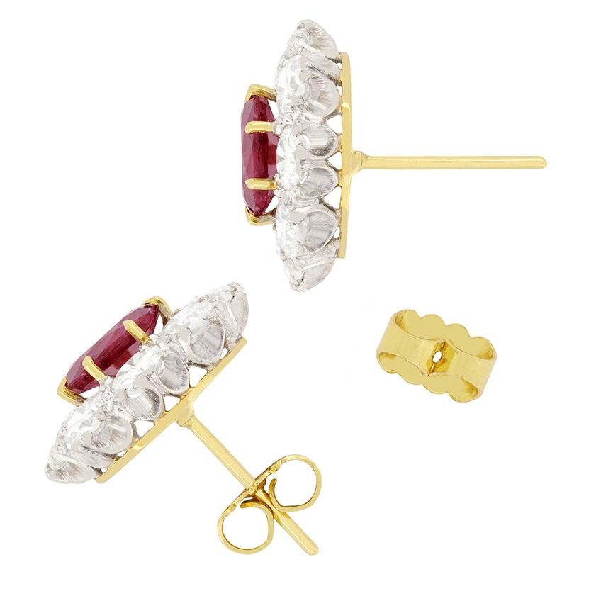 Dating to the 1950s this eye catching pair of cluster earrings feature a 1.00 carat natural ruby in each. The vibrant rubies are oval cut stones and have had some heat treatment. They are surrounded by eight 0.25 carat diamonds per ear. The round