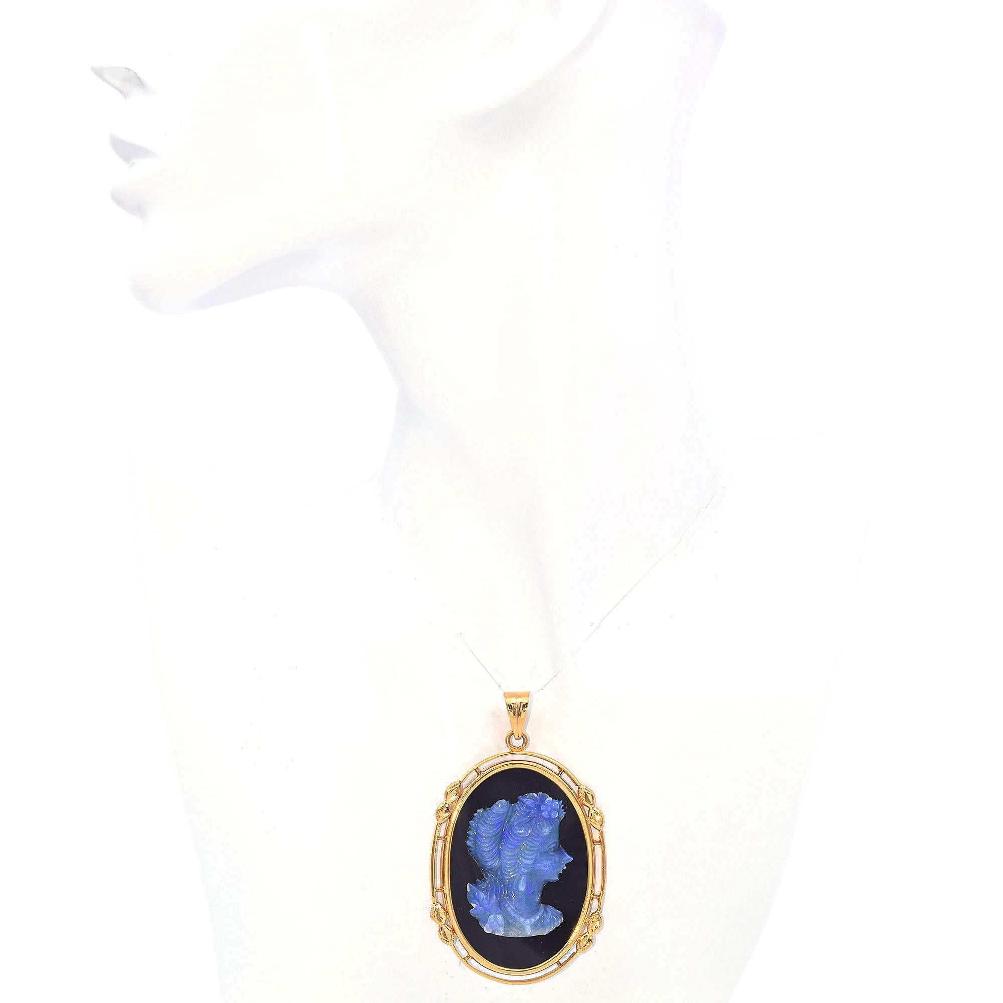 This pendant features a detailed blue opal cameo set against a deep black background. The intricate carving showcases a profile with flowing hair and delicate features. Encased in a warm gold frame, the design is accented with subtle leaf motifs on
