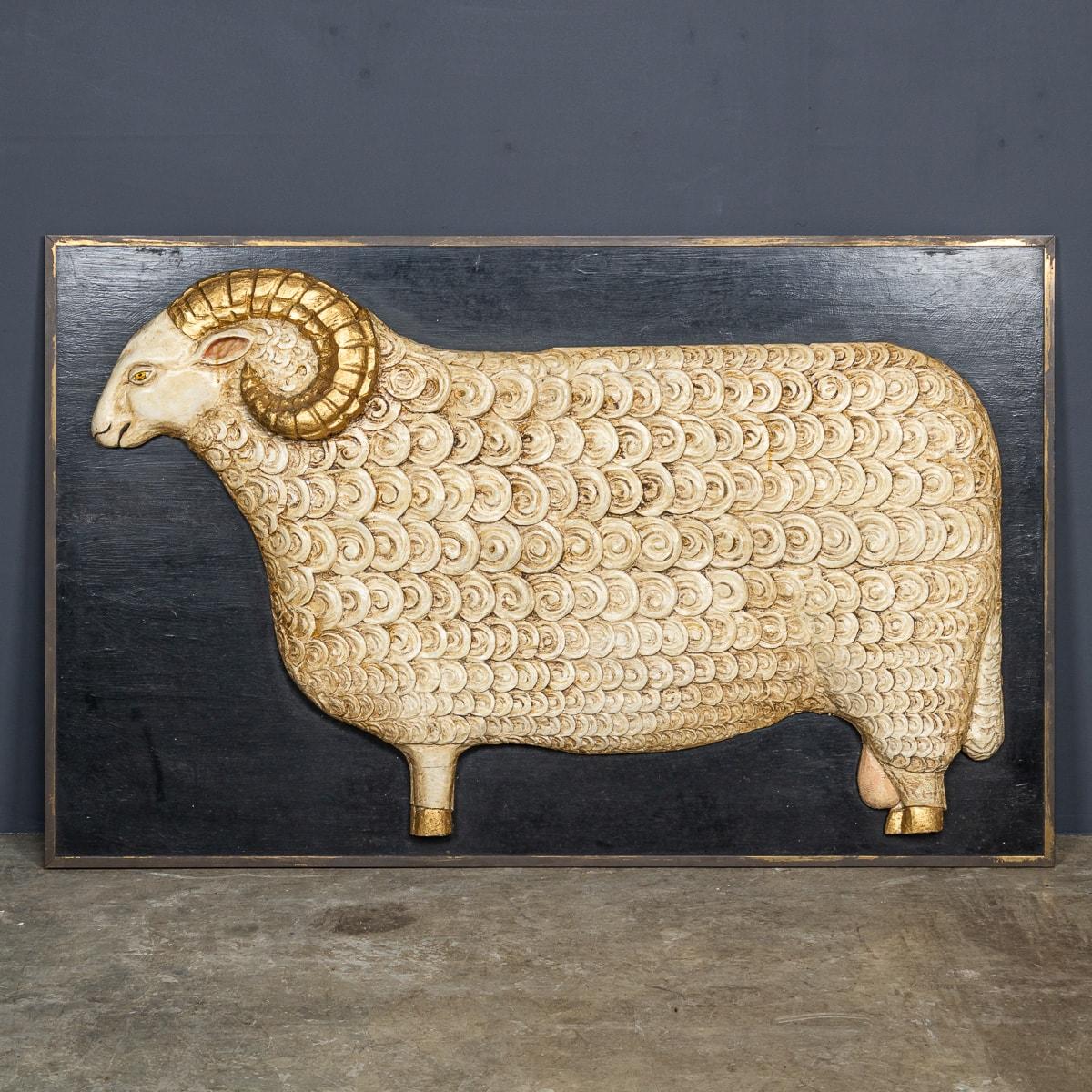 A Vintage 20th Century wooden sign depicting a ram. This painted sign is adorned with a thin brass frame surrounding the edge, accentuating the golden horns on the ram. Originating from a wool shop in the English Cotswolds, it carries a rich history