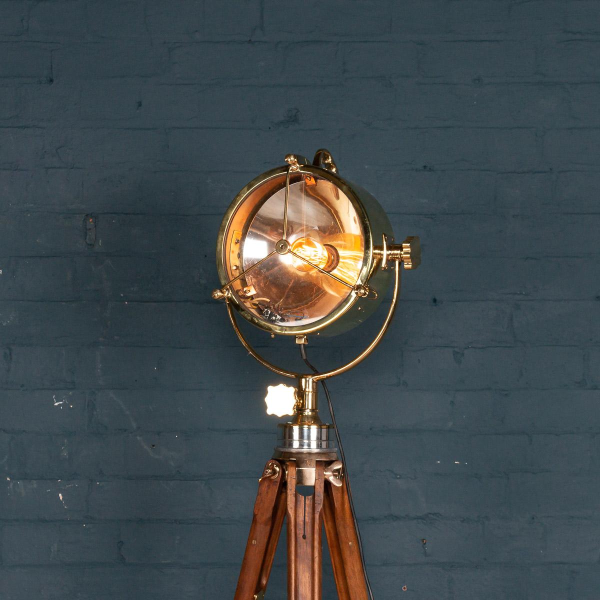 A fantastic mid-20th century English naval searchlight, mounted on an earlier 20th century tripod. These lamps would have been mounted on military or shipping vessels. With a contemporary squirrel cage light bulb, this example has been