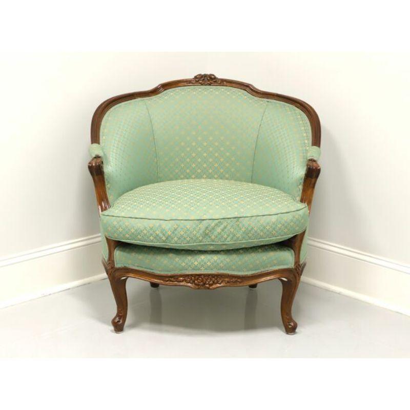A French Louis XV style Bergere armchair. Walnut frame with light green & gold fabric upholstered back, arms and seat. Features carvings to crest rail, arms, apron and curved legs. Likely made in the USA, in the mid 20th Century.

Measures: 
