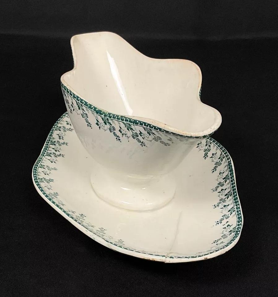 This vintage 20th-century porcelain gravy boat from Gien, featuring the elegant Montagny floral design, is a beautiful example of French ceramic artistry. Measuring 4.1 inches (10.5 cm) in height, 10 inches (25.5 cm) in length, and 6.5 inches (16.5