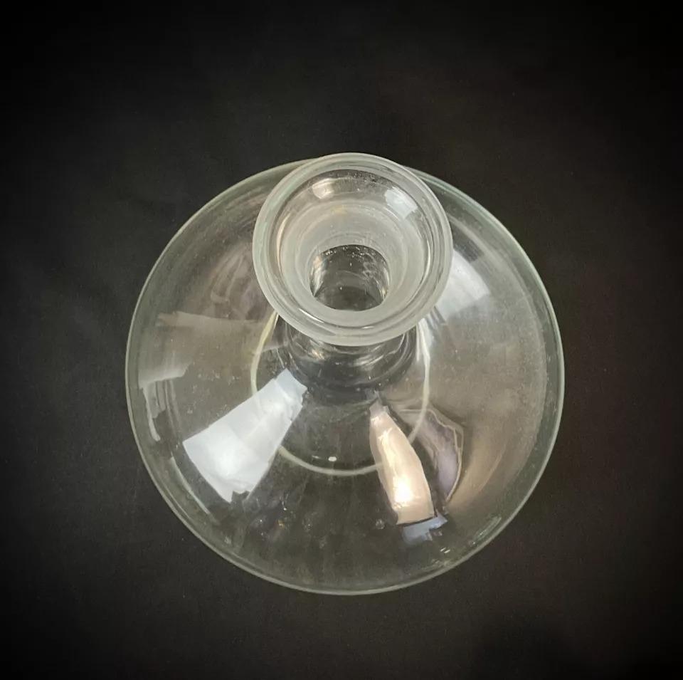 Vintage Glass Wine Decanter
This is a vintage glass wine decanter from the 20th century. The decanter has a classic form with a wide, bulbous body and a long, narrow neck, designed to aerate and serve wine. The piece is complete with its original