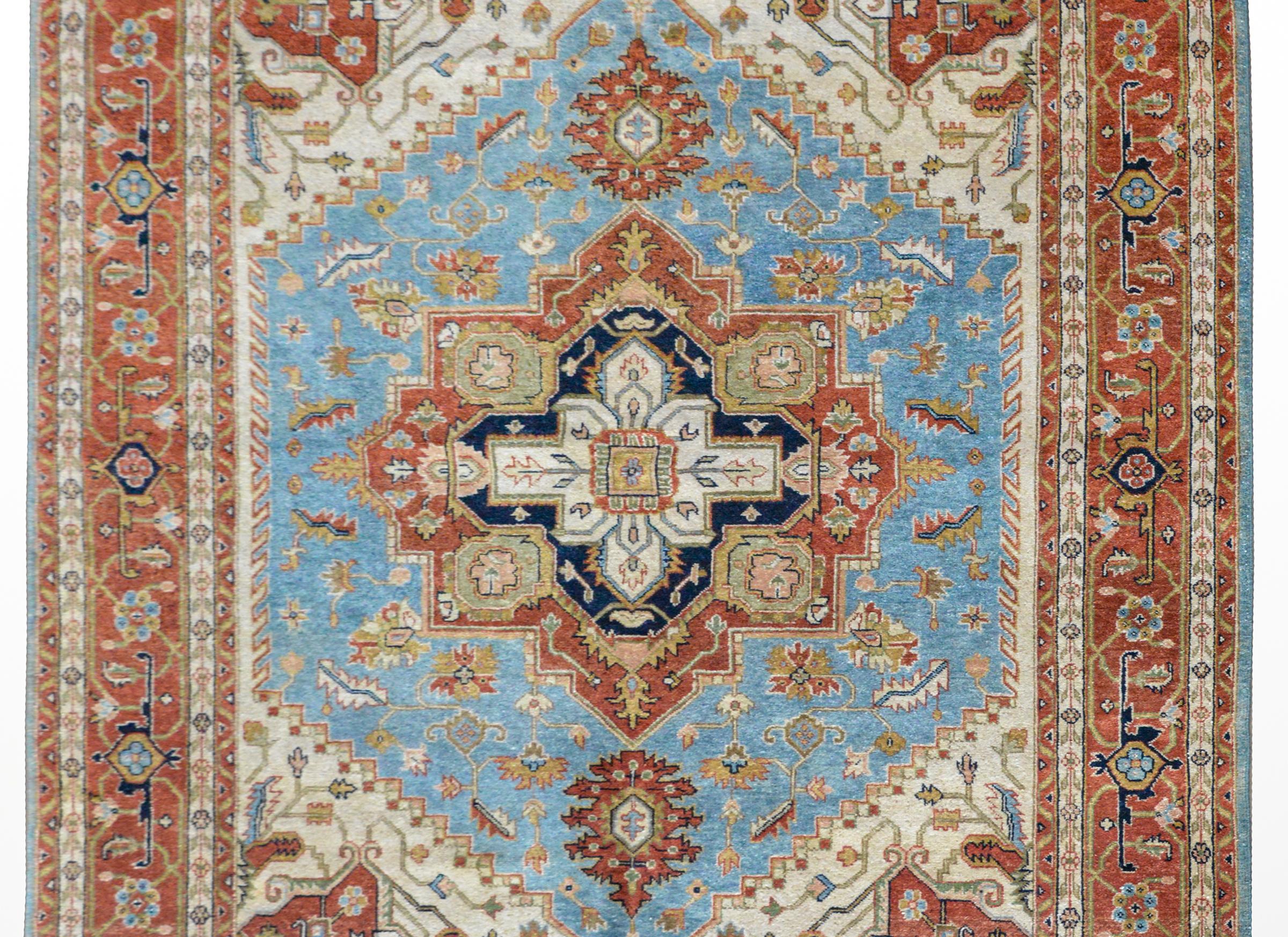 A beautiful hand knotted Indian Heriz-style rug with a traditional pattern containing a large central floral medallion woven in burnt orange, ochre, dark indigo, and pink, against a field of flowers set against a light indigo background. The border