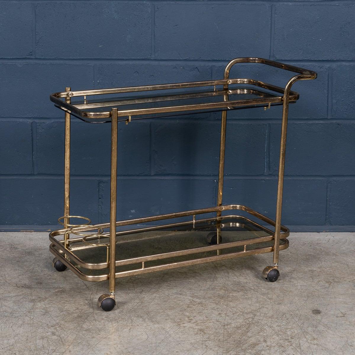 Questo carrello portabevande del XX secolo vanta uno splendido effetto ottone con una robusta struttura in ottone, esemplificando l'eleganza del design italiano contemporaneo della seconda metà del secolo scorso. La sua struttura a due livelli