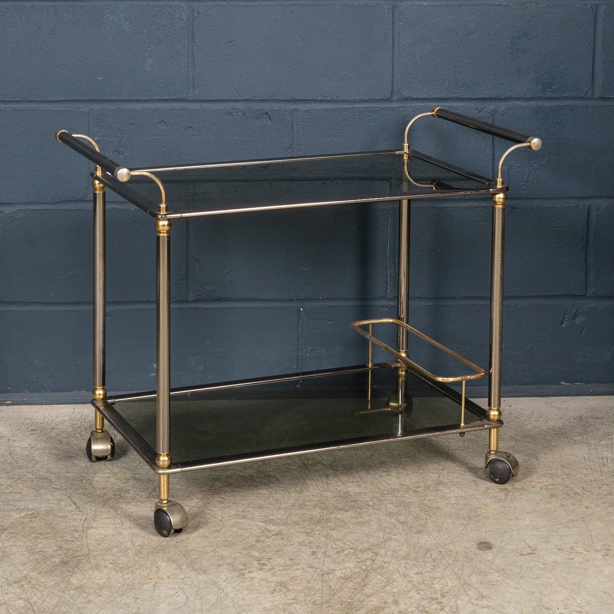 This 20th Century drinks trolley boasts a brushed steel and brass frame, exemplifying the elegance of contemporary Italian design from the second half of the last century. Its two-tier construction features a versatile arrangement of shelves,