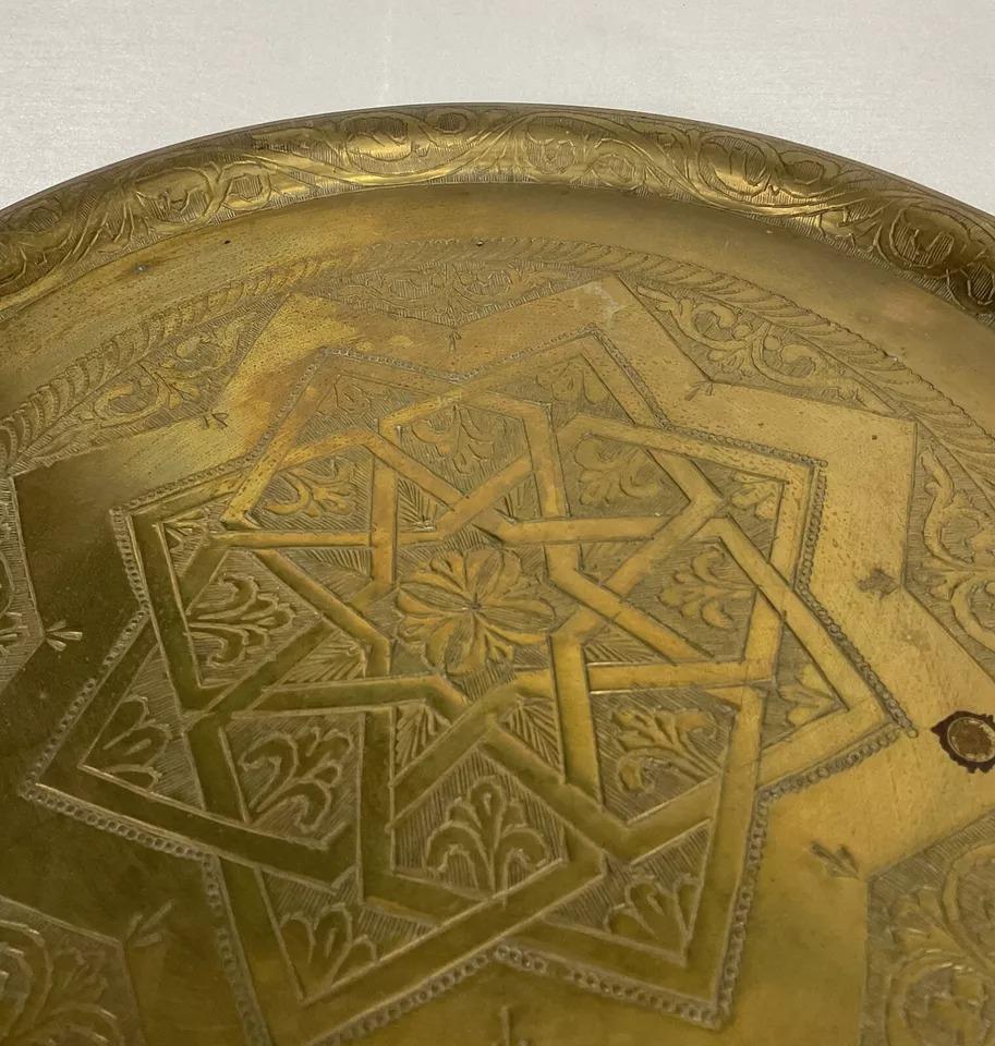 This vintage 20th-century large oriental brass plate showcases exquisite craftsmanship with intricate floral engravings. Measuring 13.6 inches (34.5 cm) in diameter and weighing 1.77 lbs (803 g), this piece is both decorative and functional. Its
