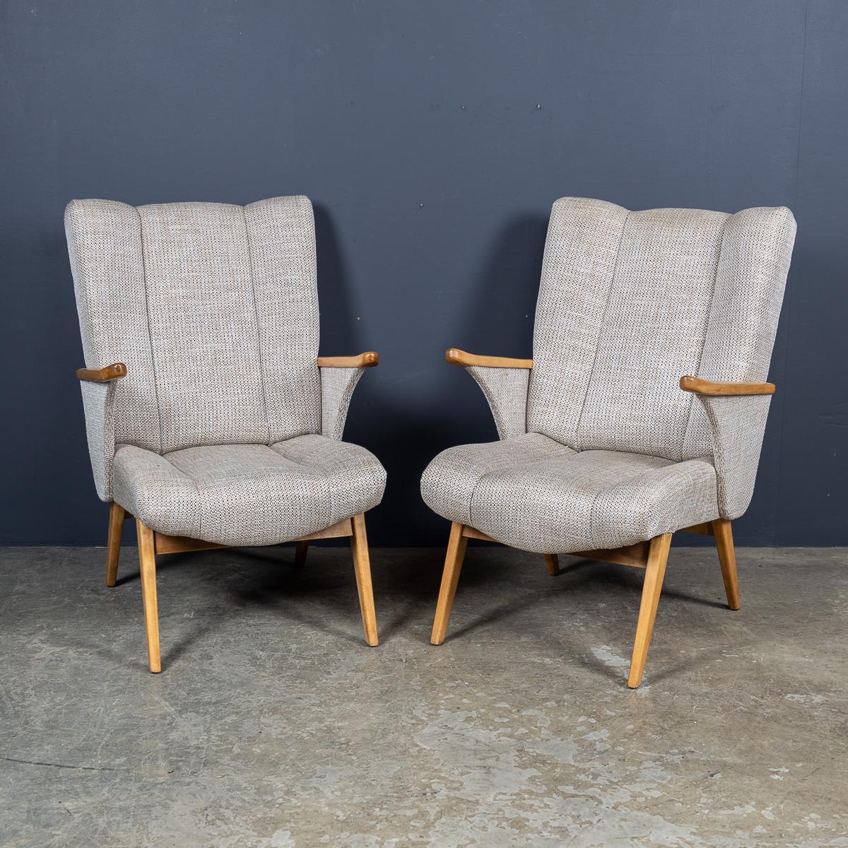A 20th Century pair of winged armchairs by Gelenka of Germany, a company associated with the Bauhaus movement and noted for including Erich Dieckmann among its designers. Crafted in beech, this pair has been reupholstered in a neutral woven