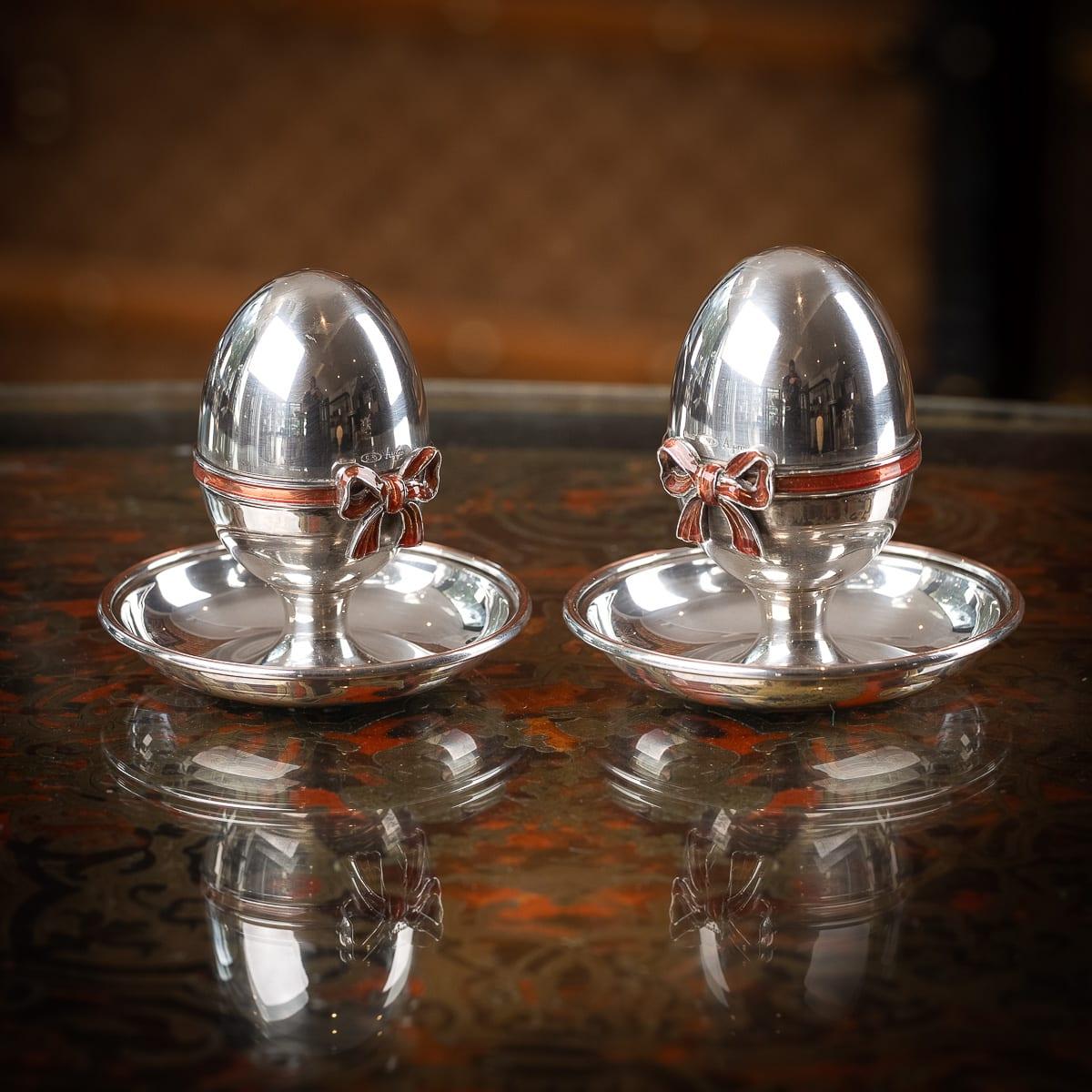 A 20th Century Italian solid silver pair of egg cups, retailed by Asprey of London. Each egg cup features a removable lid, adorned with an enamelled bows mounted to the rim. Set on a circular base, the design allows the eggshell to be easily broken