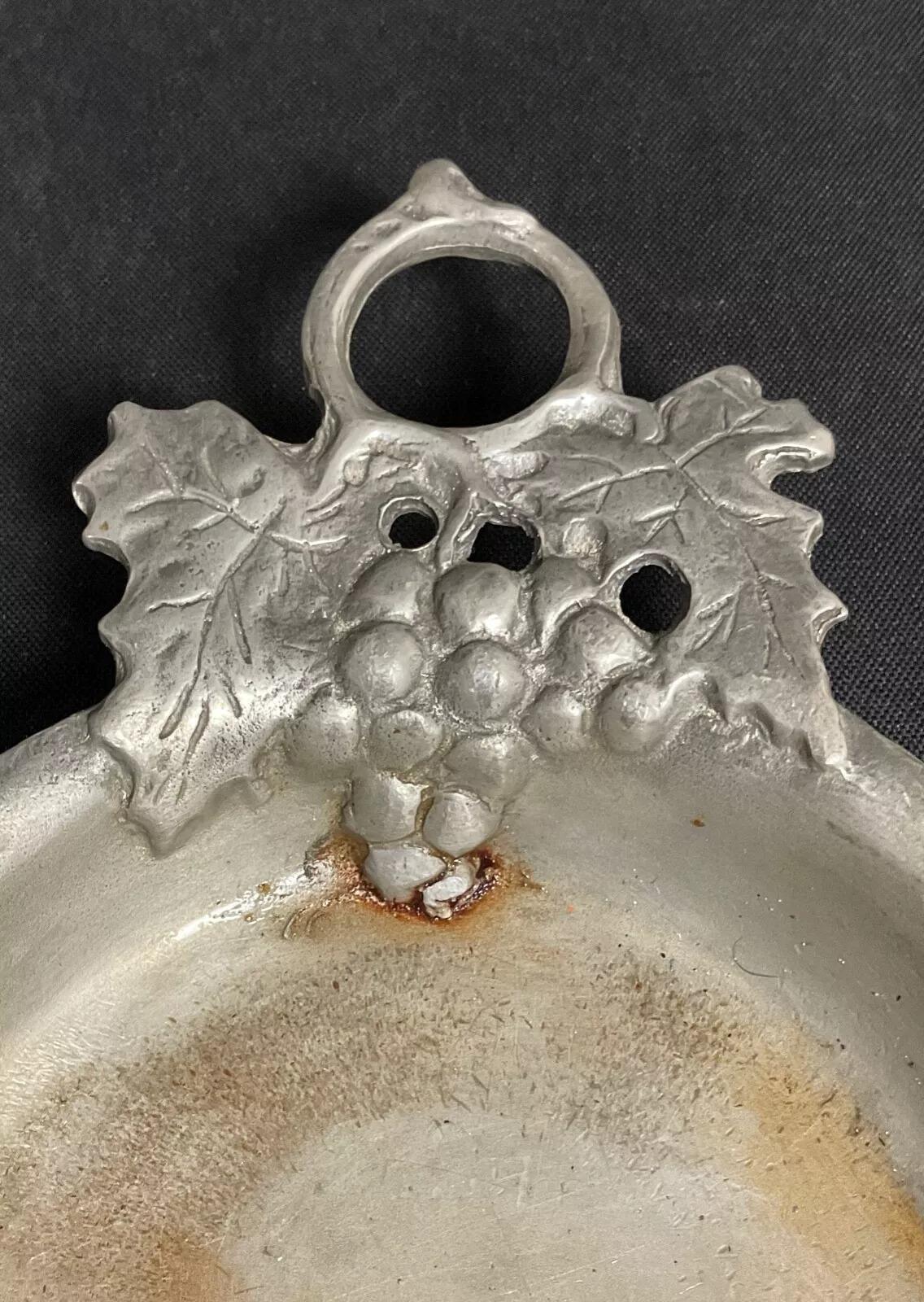 Questo affascinante tastevin in peltro del XX secolo, caratterizzato da un intricato motivo di uva e da un marchio (non identificato), è un vero e proprio pezzo di tradizione enologica francese. Con un'altezza di 2,5 cm, un diametro di 11,5 cm, una