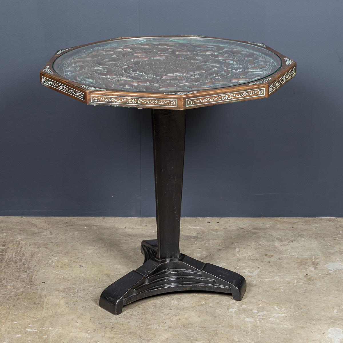 A superb 20th Century Spanish cast iron pedestal table with three feet, supporting a nonagon (nine-sided) copper top embossed with swimming fish and finished with a protective glass cover. Signed Malart Spain.

Malart Spain was a decorative arts
