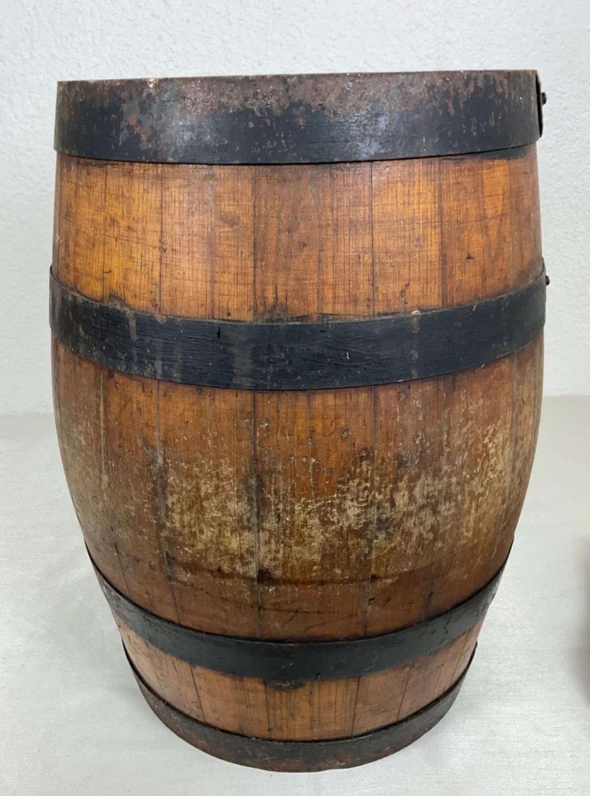 This vintage 20th-century wooden barrel with forged iron bands is a charming decorative piece, showcasing traditional woodworking techniques. Resting on its original wooden stand, the barrel measures 15.2 inches (38.5 cm) in height and 11.6 inches