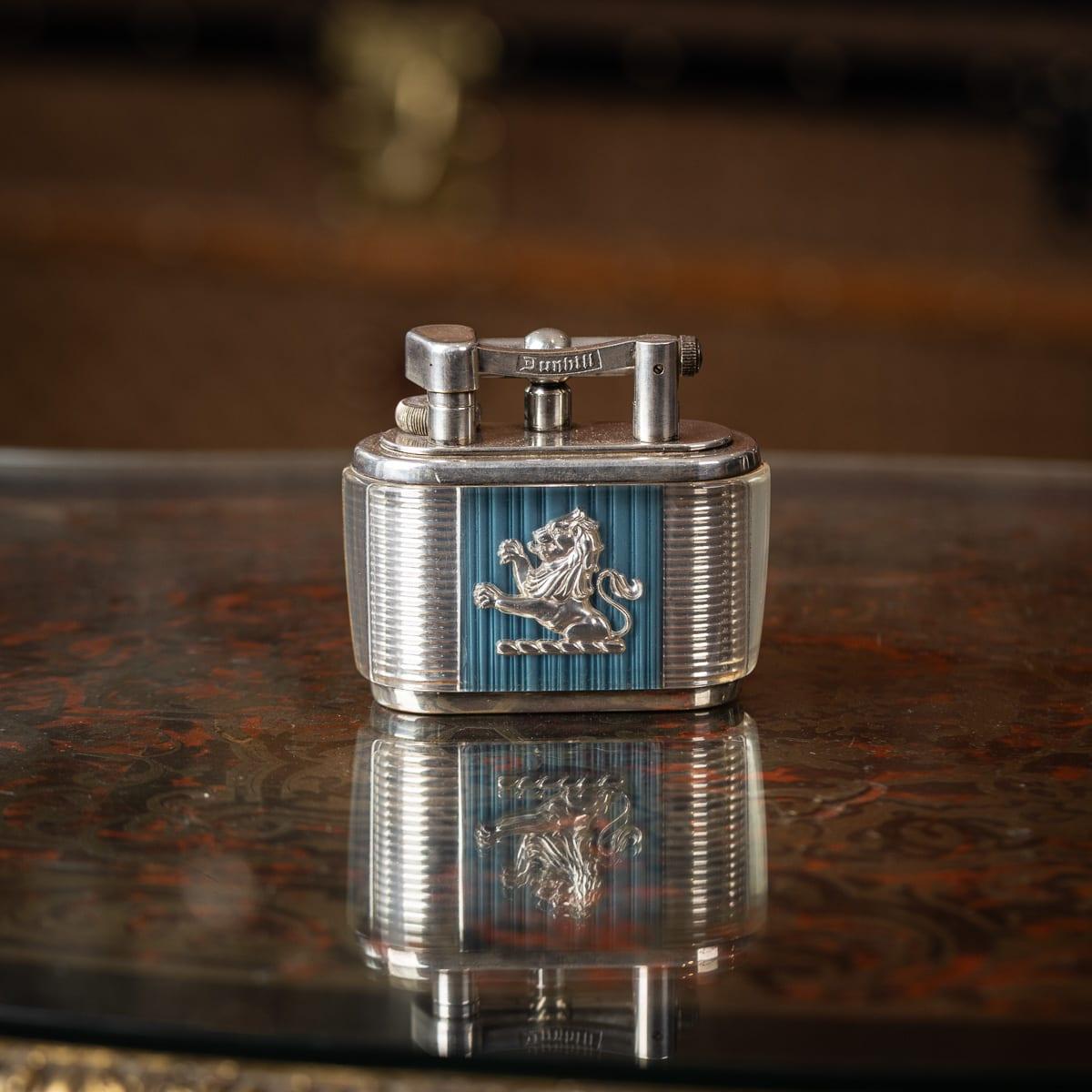  Accendino da tavolo Dunhill Half-Giant Joseph Lucas della metà del XX secolo. Realizzato in forma rettangolare curva con montature placcate in argento, questo pezzo presenta due leoni rampanti su un fondo a coste blu e argentato all'interno di una