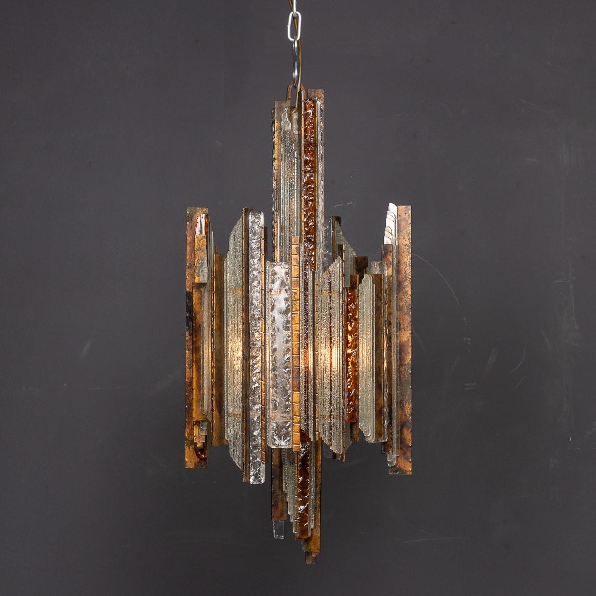 A 20th-century brutalist chandelier by Albano Poli, designed and crafted in the 1970s. Featuring an iron base, it is elegantly adorned with clear and amber glass accents. This four-bulb pendant light is a monumental piece, combining illumination
