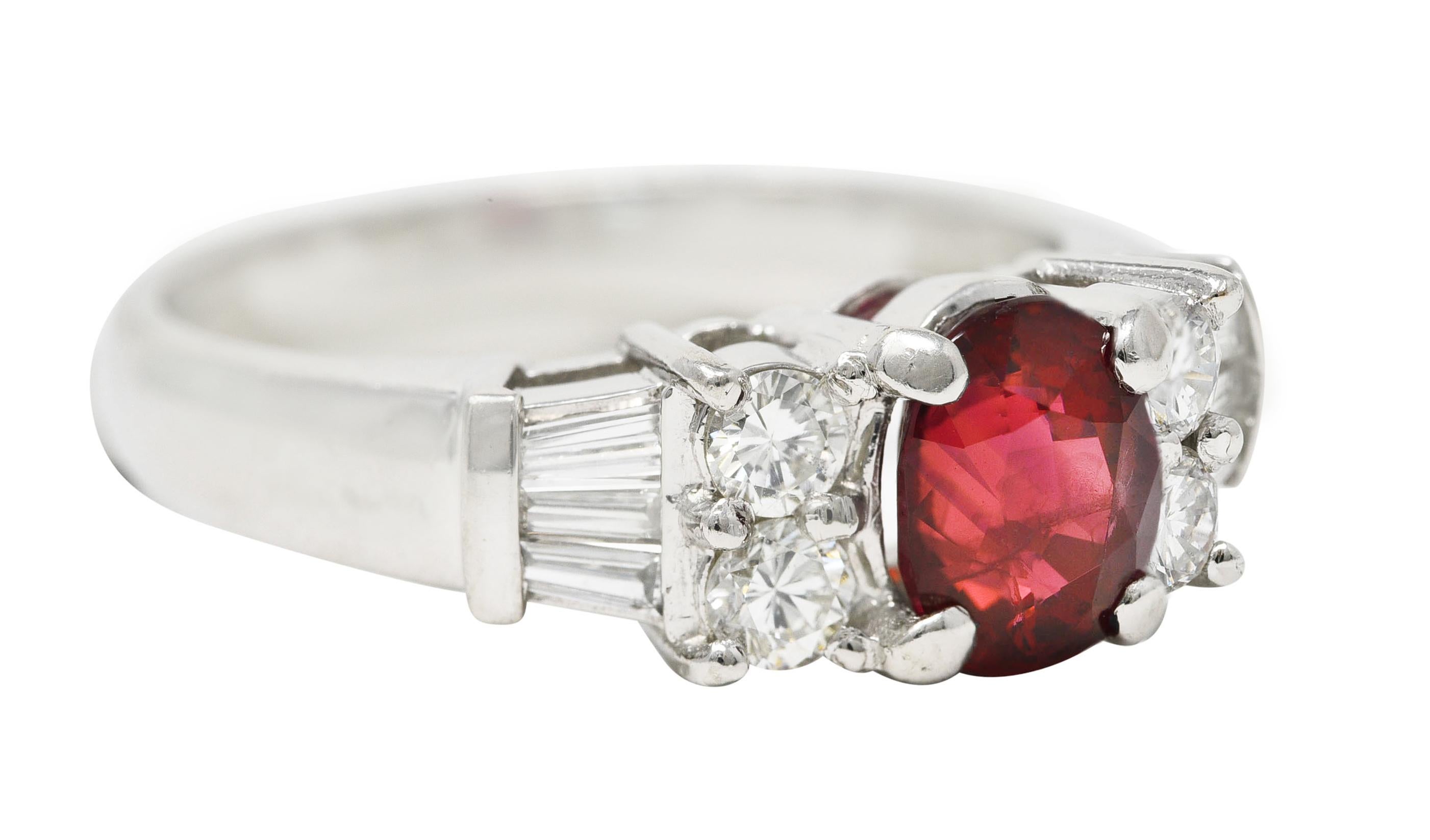Centering an oval cut ruby weighing 1.54 carats total - transparent medium red in color. Natural Thai in origin - prong set in basket and flanked by diamond cluster shoulders. Comprised of round brilliant and tapered baguette cut diamonds prong set.