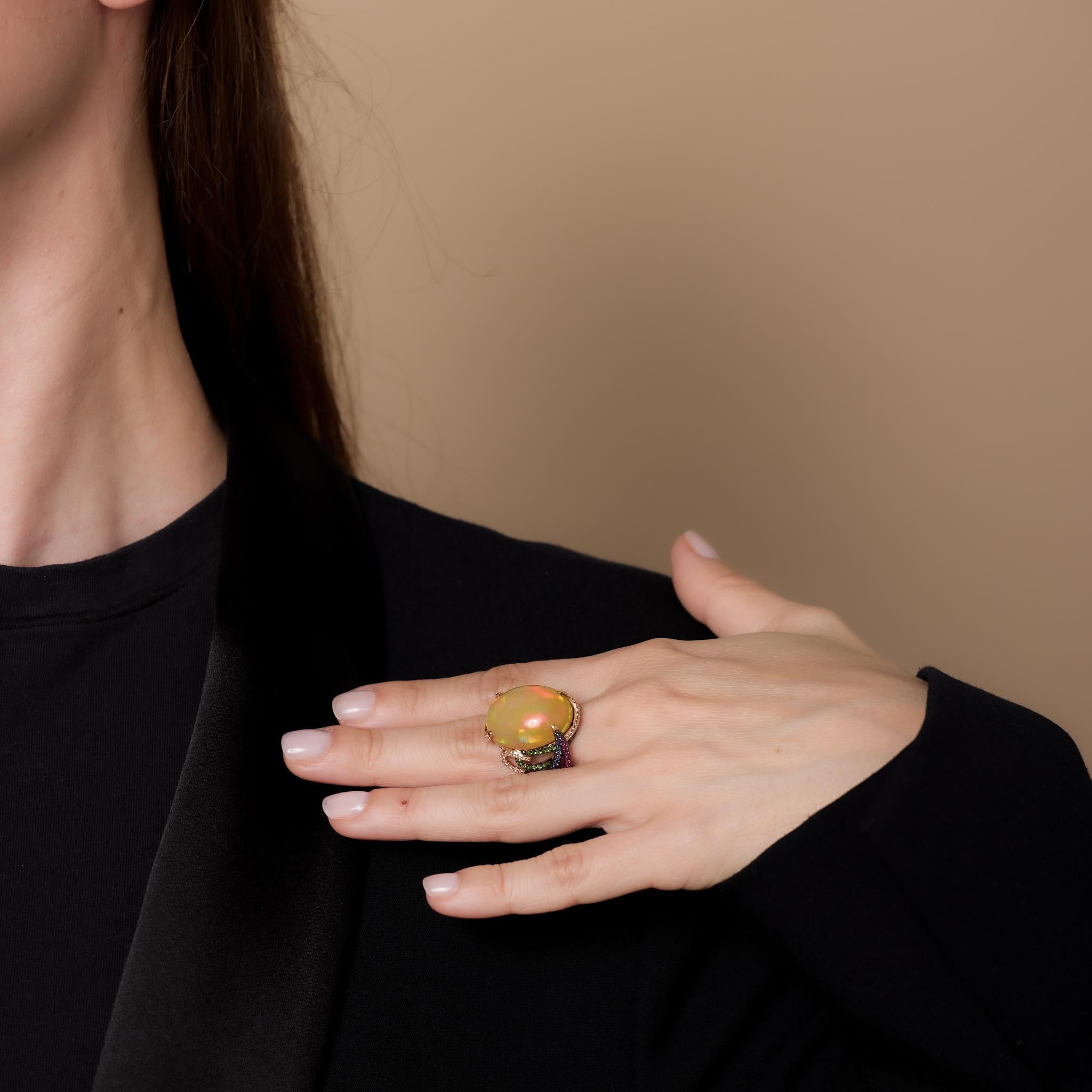 This vintage 18k rose gold cocktail ring showcases a 21.70-carat cabochon cut opal, accented by 52 rubies, 49 tsavorite, 44 round brilliant diamonds, and 30 sapphires totaling 1.50 carats. Crafted in the 1990s, it is hallmarked with a purity mark