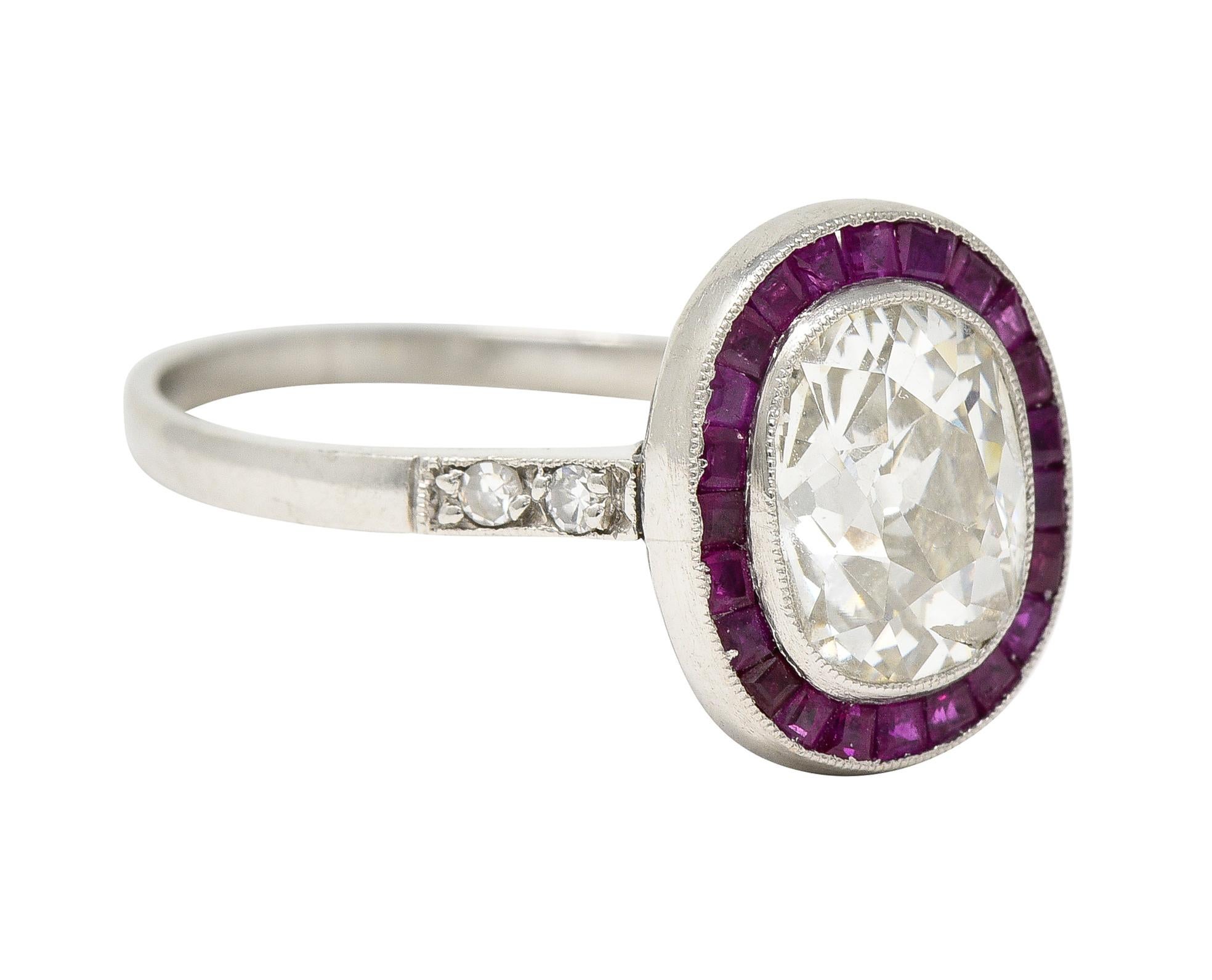 Centering an old mine cut diamond weighing. approximately 1.96 carats - K color with I1 clarity. Bezel set with a halo surround of calibré cut rubies weighing approximately 0.24 carats total. Transparent medium purplish red in color - channel set.