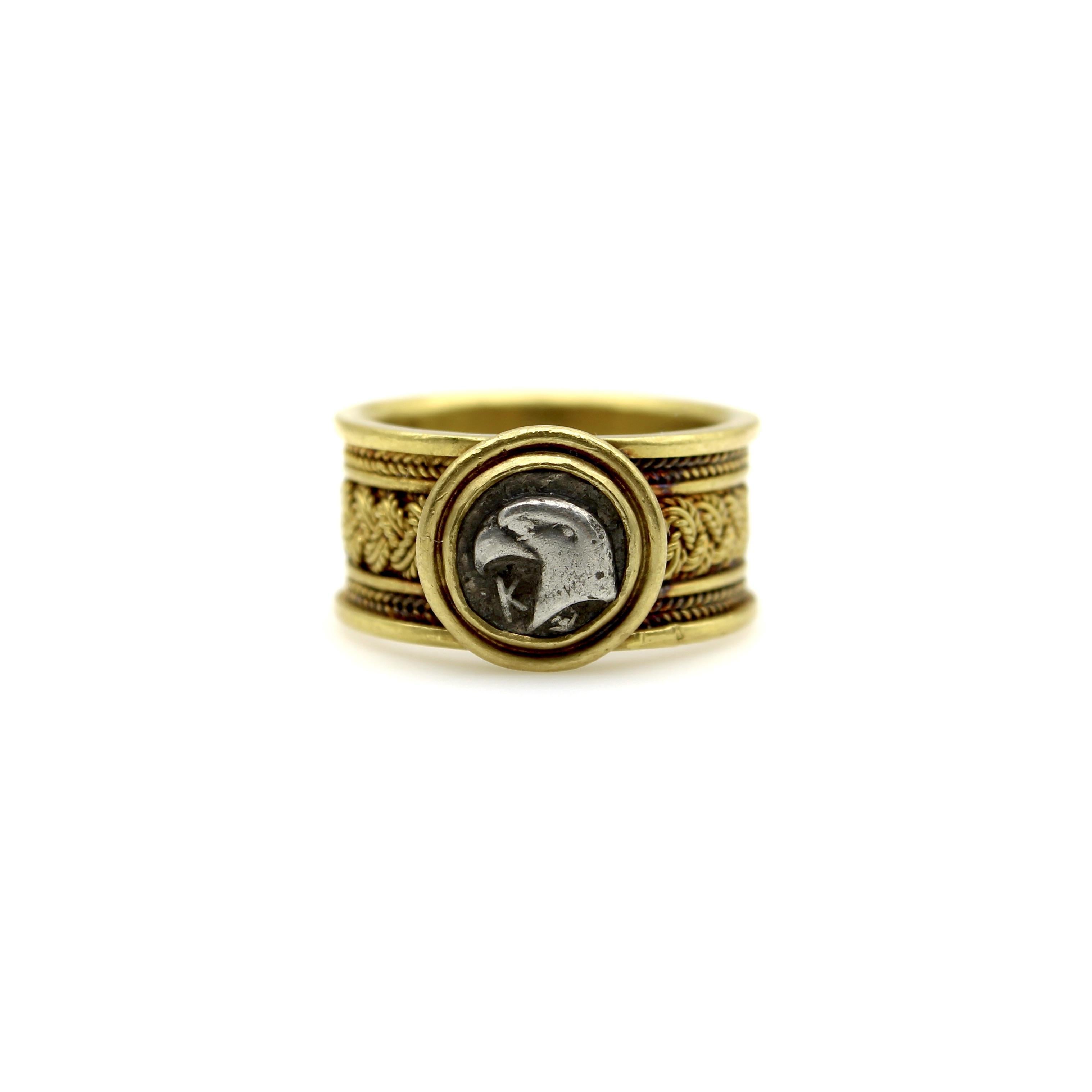 This 22k gold ring contains a striking ancient coin in a wirework band that mirrors the antiquity of the coin. The coin has the face of either an eagle or falcon, with the Greek letter K next to it. The mount has an opening so that the coin can be