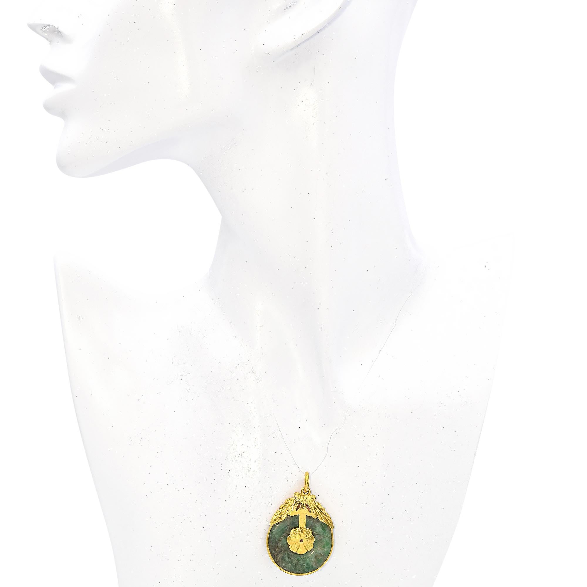 This piece features a round jade stone with a rich green hue. The jade is elegantly encased in a detailed yellow gold setting, showcasing intricate leaf and floral motifs.

Weight: 11.6 grams
Stone: Jade (25 mm)
Pendant: 34.5 mm x 26.25 mm
Metal: