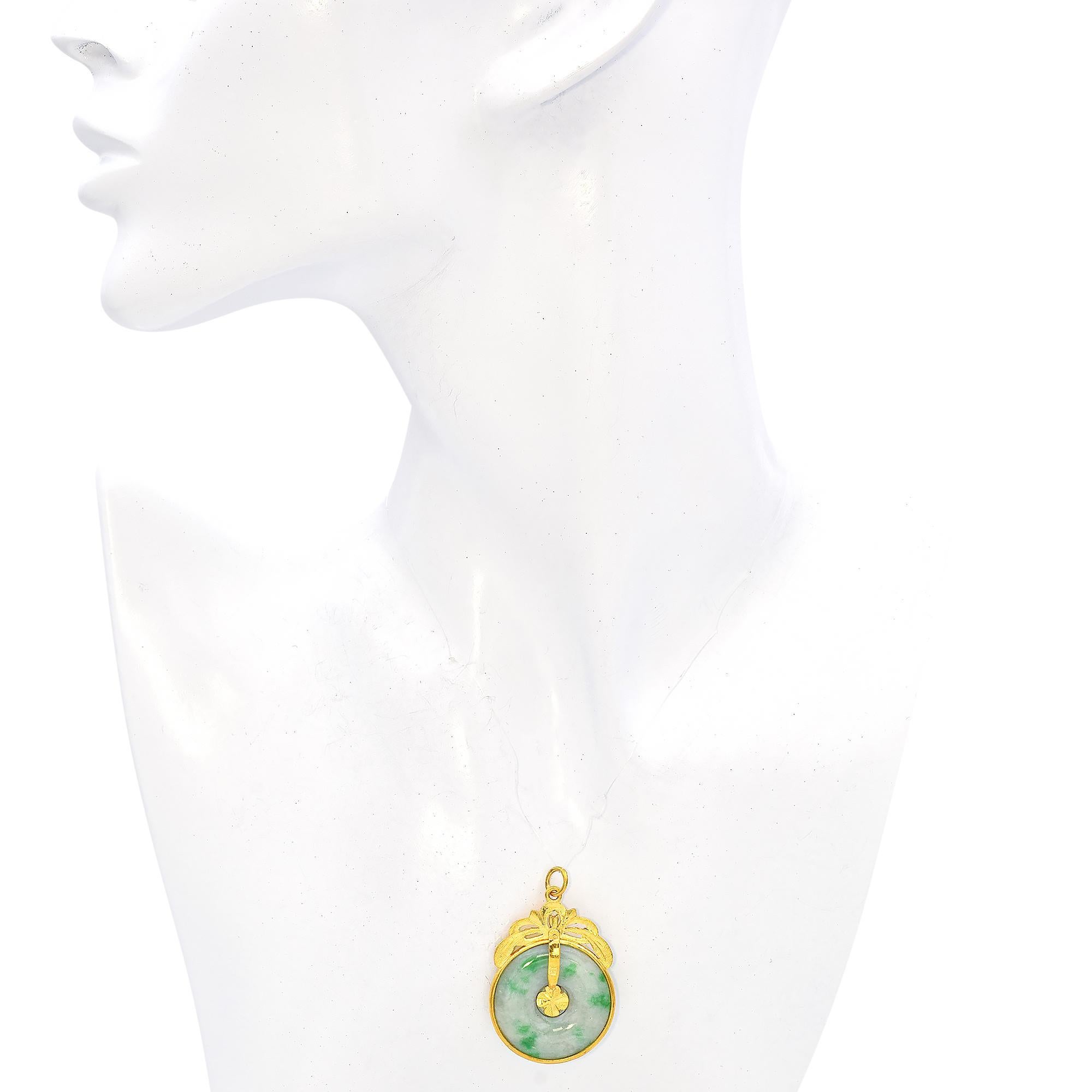 A refined pendant featuring a circular jade disc with subtle green hues, elegantly framed in 23k yellow gold. The design includes a delicate floral motif at the top, enhancing its sophisticated appeal.

Weight: 10.3 grams 
Stone: Jade