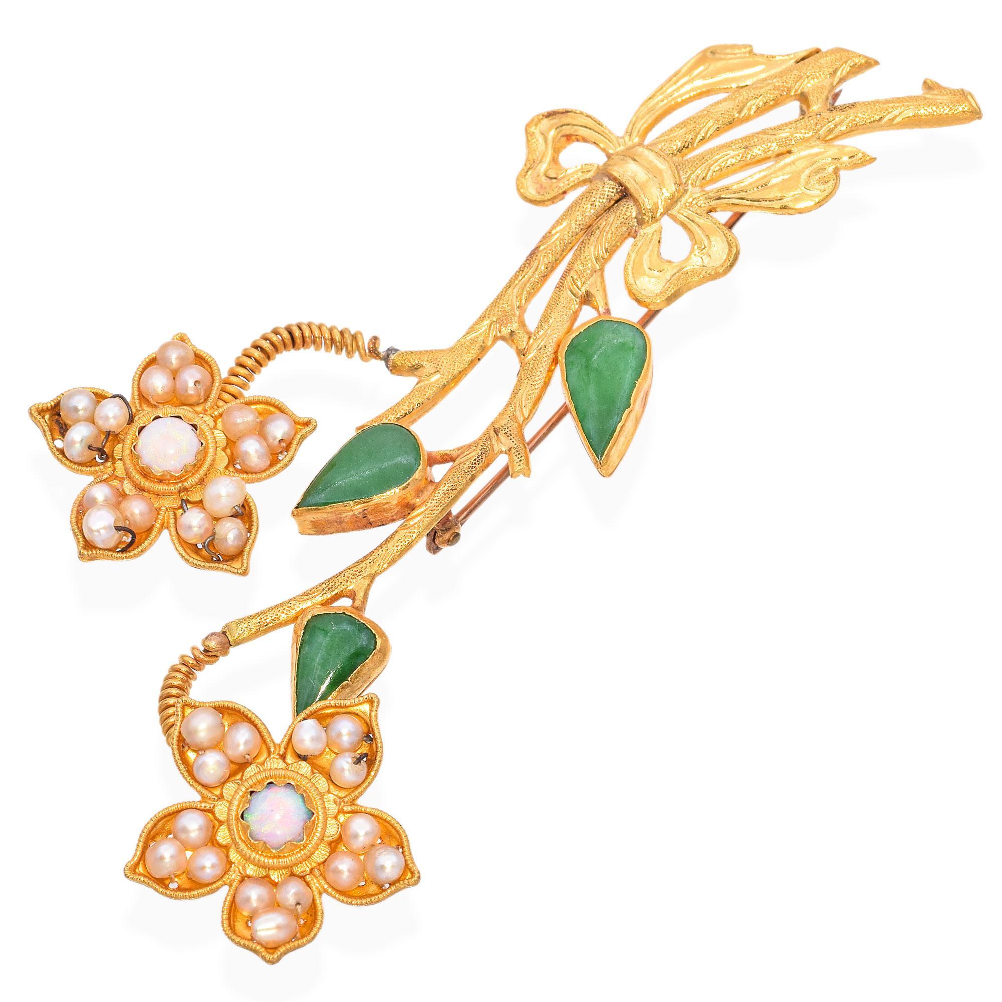 Cette exquise broche florale est finement travaillée en or. La broche présente deux motifs floraux ornés de perles et d'opales au centre. Les pétales sont ornés de petites perles.
La tige est rehaussée de Jade vert en forme de goutte d'eau. La